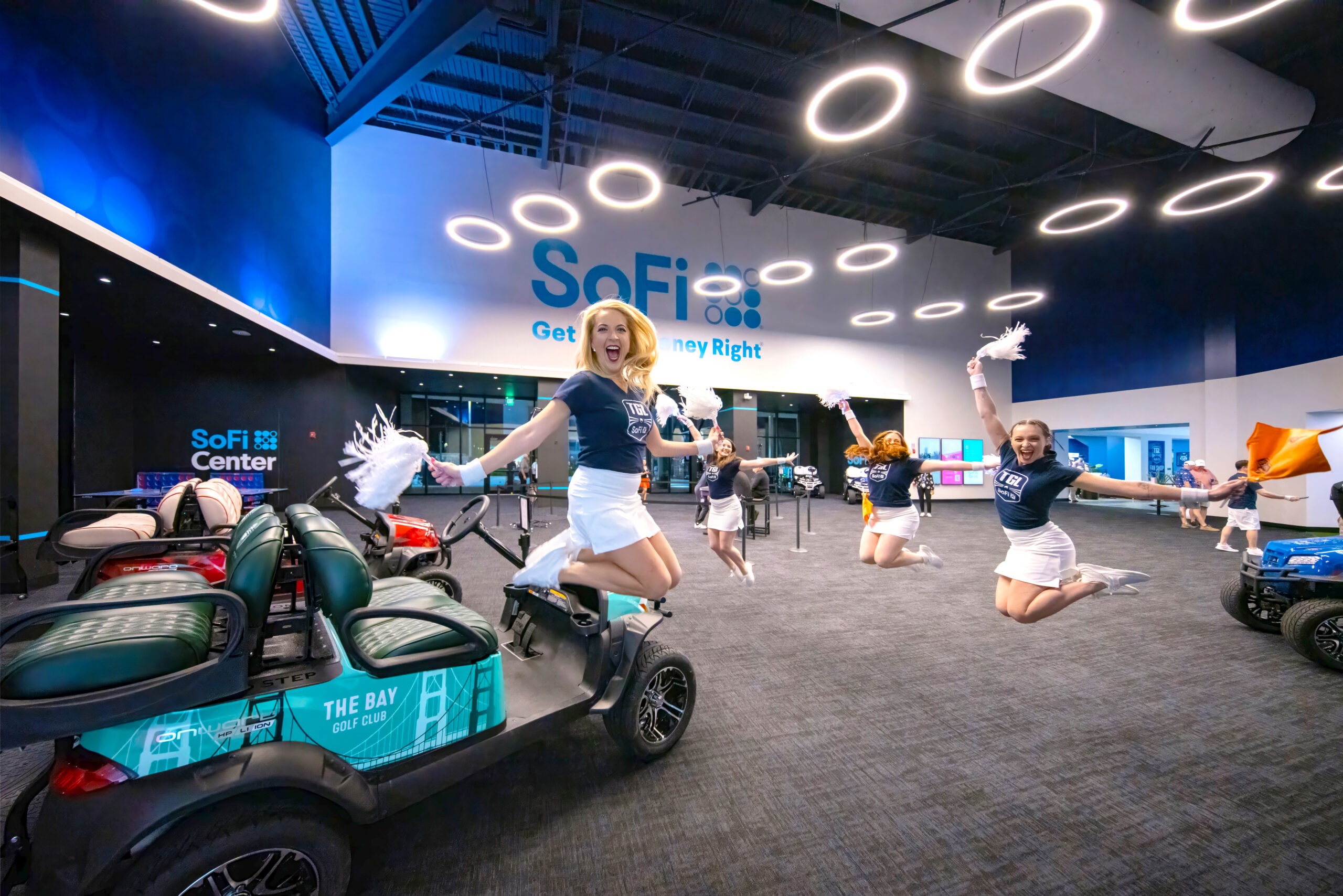 Professional cheerleaders leap midair inside the SoFi Center at the TGL arena in Palm Beach, Florida — a vibrant moment of energy and celebration captured by David Scarola, official photographer for Pinpoint Media and TGL global events.David Scarola Photography, TGL photographer, Pinpoint Media, SoFi Center Palm Beach, worldwide event photographer, global brand photographer, corporate photographer Florida, international media photographer, commercial event photographer, luxury brand photography, elite event coverage, worldwide brand storytelling, corporate media coverage, global marketing photography, world-class event photography.