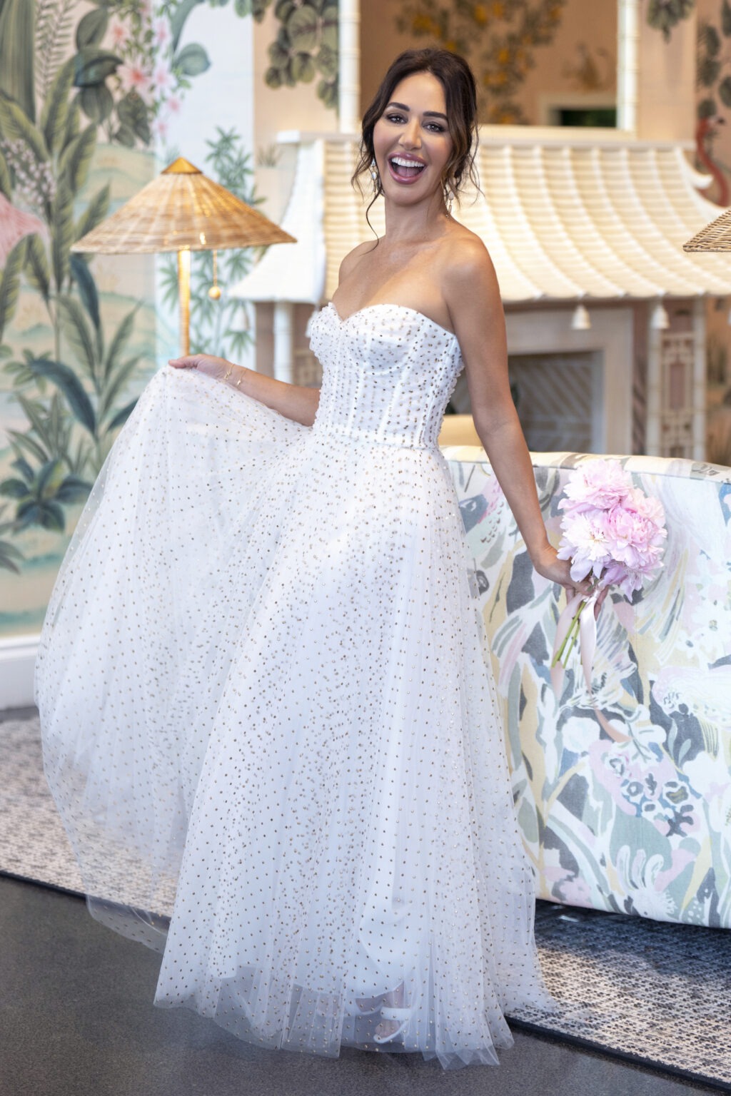 Radiant bride laughing in the lobby of The Colony Hotel, Palm Beach Island — wearing a modern strapless beaded gown and holding soft pink peonies. Captured by David Scarola Photography, a luxury wedding photographer in Palm Beach known for cinematic lighting, editorial composition, and timeless emotion. Fine-art wedding portrait featuring vibrant interior design, tropical elegance, and authentic joy in a world-class destination setting.