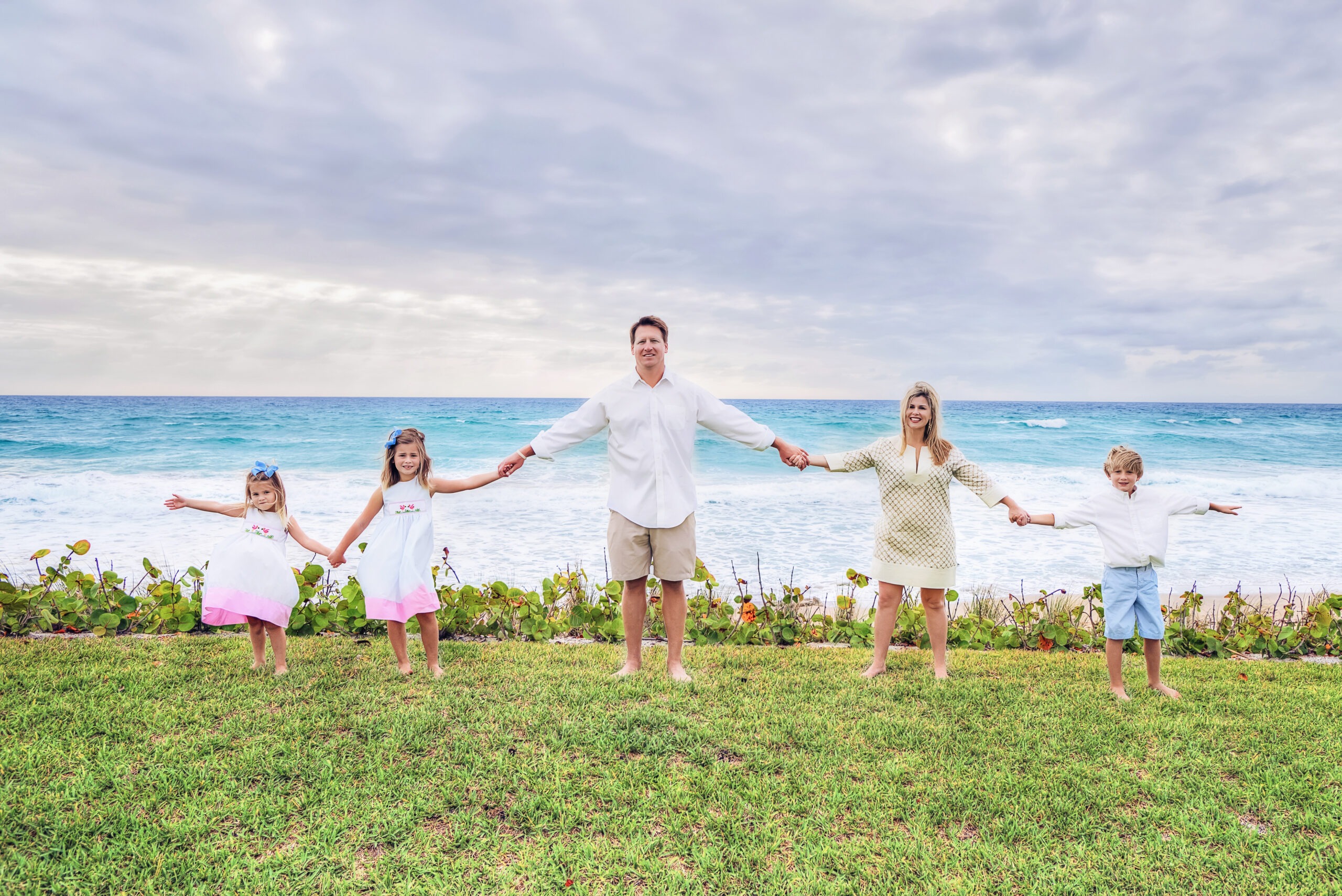 Mom and dad holding hands together with their 3 children, connected in love and happiness as family photographer, David Scarola, leads the family through a 75 minute long family portrait shoot in North Palm Beach Florida in the famed golf, tennis and beach community of Lost Tree Village.