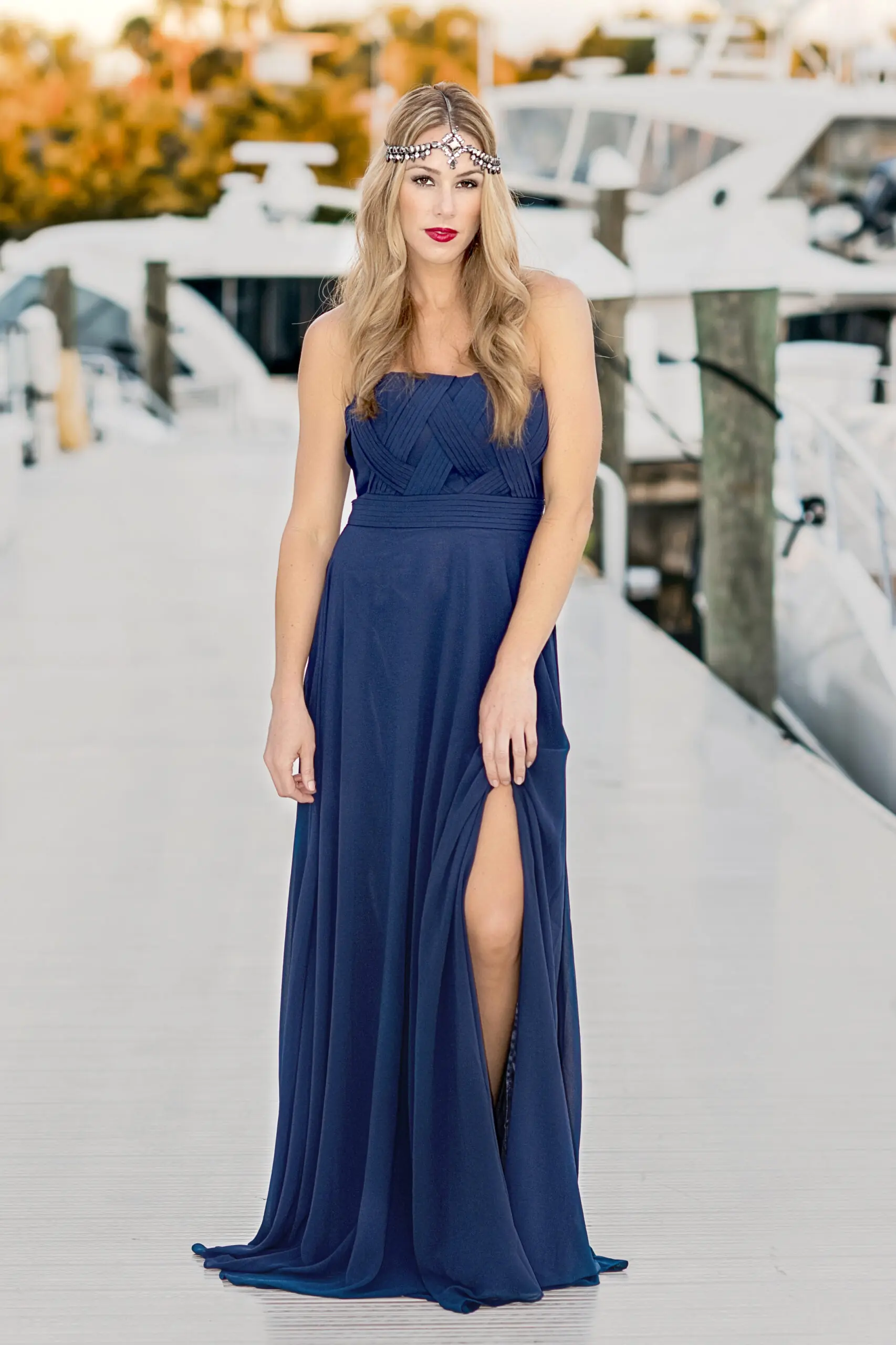 High-fashion lifestyle photograph of a model wearing a navy blue evening gown and jeweled headpiece during a Ceci Palm Beach boutique marketing campaign, photographed by David Scarola at the Admirals Cove Country Club on Jupiter Island, Florida. The model stands elegantly on a marina dock surrounded by luxury yachts at golden hour, capturing the refined elegance and coastal glamour of the Ceci Palm Beach brand.David Scarola Photography, Ceci Palm Beach, Admirals Cove photoshoot, Jupiter Island fashion photographer, Palm Beach luxury boutique photography, catalog photography Florida, women’s fashion campaign, fine art fashion photographer, lifestyle and brand photographer Palm Beach, high-end fashion marketing, luxury boutique imagery, resort fashion photography, professional branding photographer Florida, coastal elegance photography, Scarola style photography, Jupiter Florida commercial photographer, Palm Beach women’s boutique, designer fashion photographer, resortwear photography Palm Beach, Admirals Cove luxury country club photoshoot.