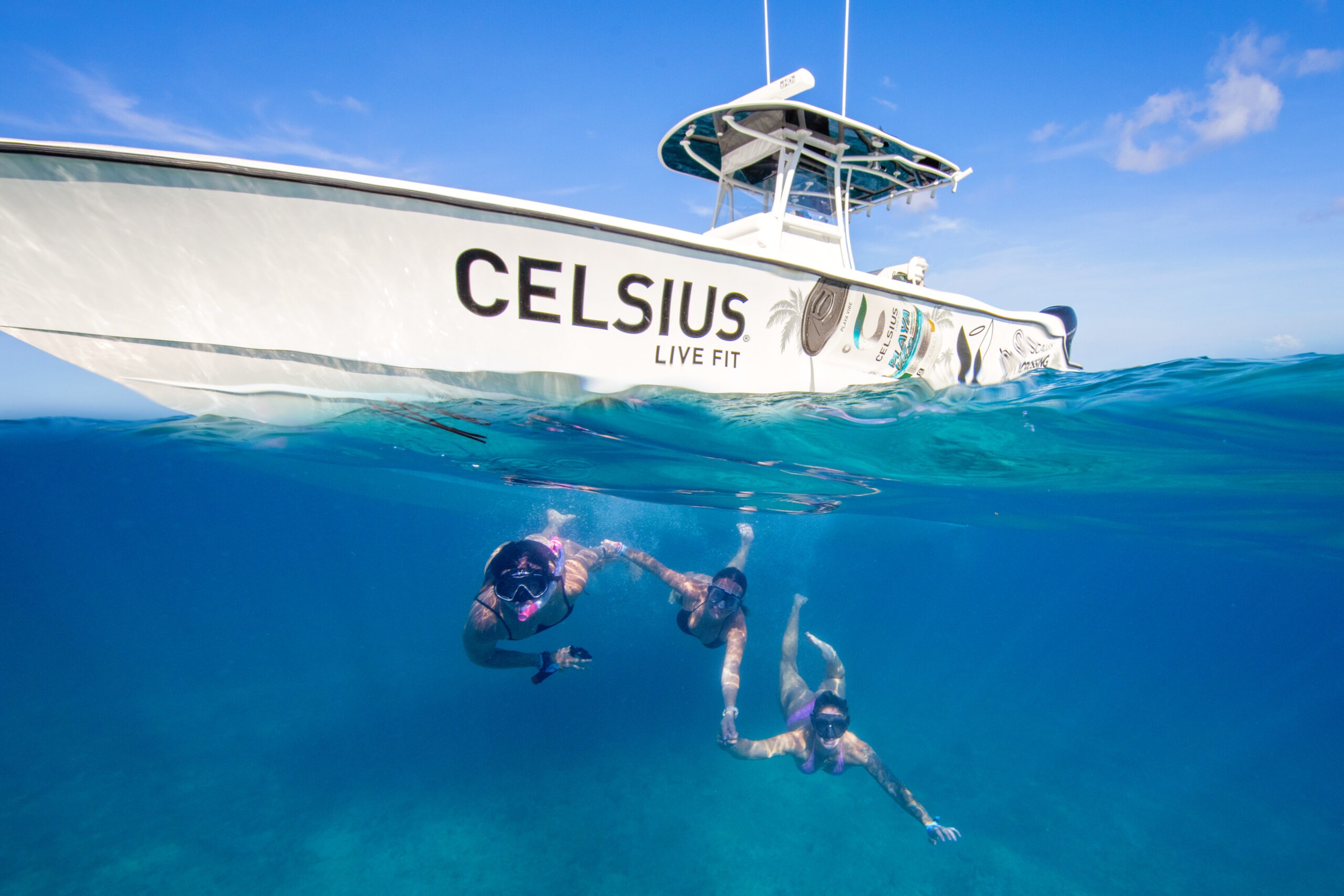 Celsius team snorkeling in the turquoise waters of Bimini, Bahamas beside their branded “Celsius Live Fit” boat during the Crossing for Cystic Fibrosis event — a vibrant underwater over/under photograph capturing the spirit of adventure and wellness.Celsius Live Fit, Crossing for Cystic Fibrosis, Pipers Angels Foundation, Bimini Bahamas photography, underwater lifestyle photography, over-under ocean photography, David Scarola Photography, corporate brand event photographer, global event coverage, fitness and wellness photography, adventure brand storytelling, luxury commercial photographer Bahamas, Florida event photographer, promotional brand shoot ocean, creative brand content photographer.