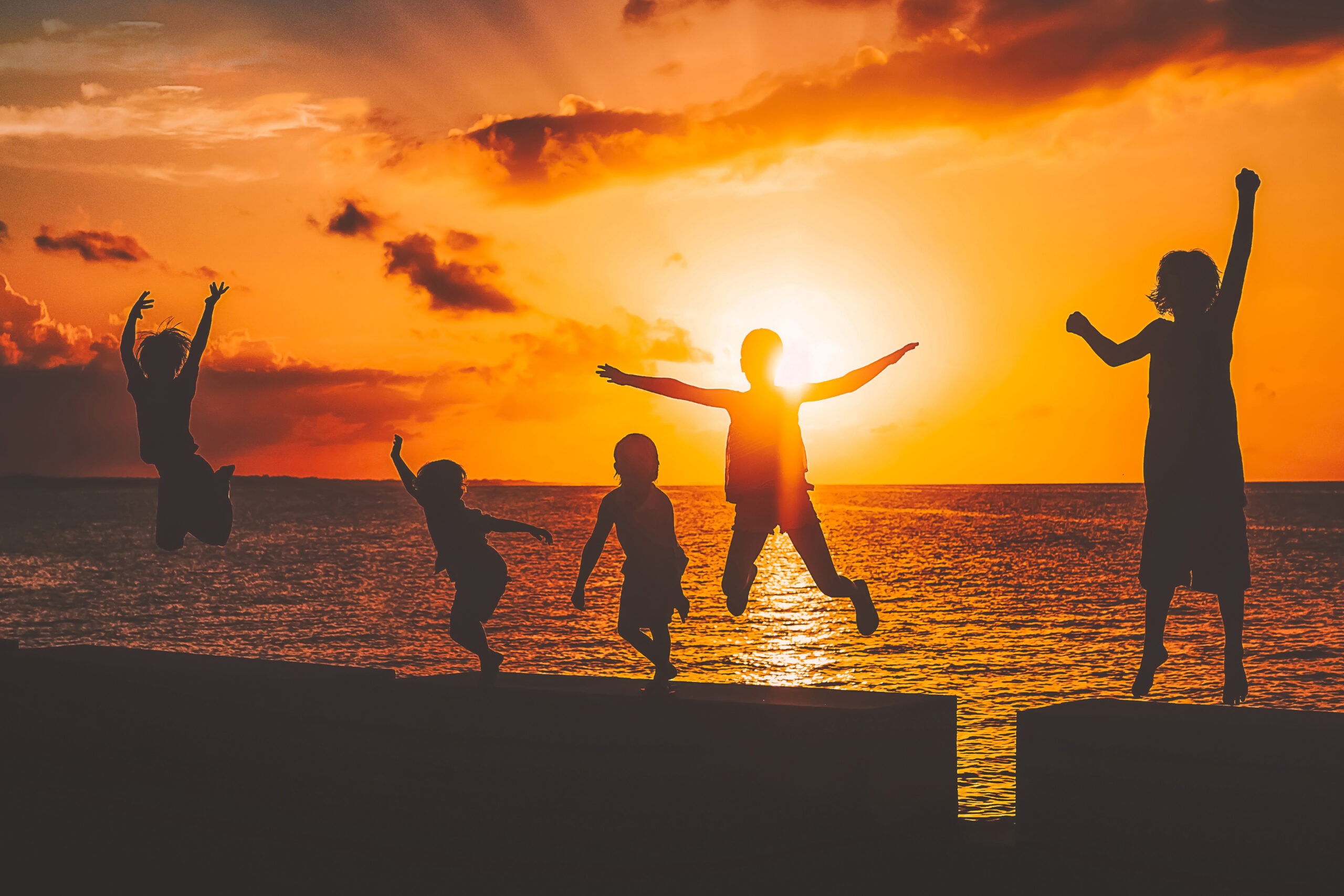 Five wonderfully happy children in the Bahamas in Marsh Harbour in the Abaco Islands jumping playfully and gleefully in the Bahamian sunset during a family photo shoot with master family photographer, David Scarola, who travels to the Bahamas 4 times each year from his Jupiter Florida home for family photo shoots throughout the islands.