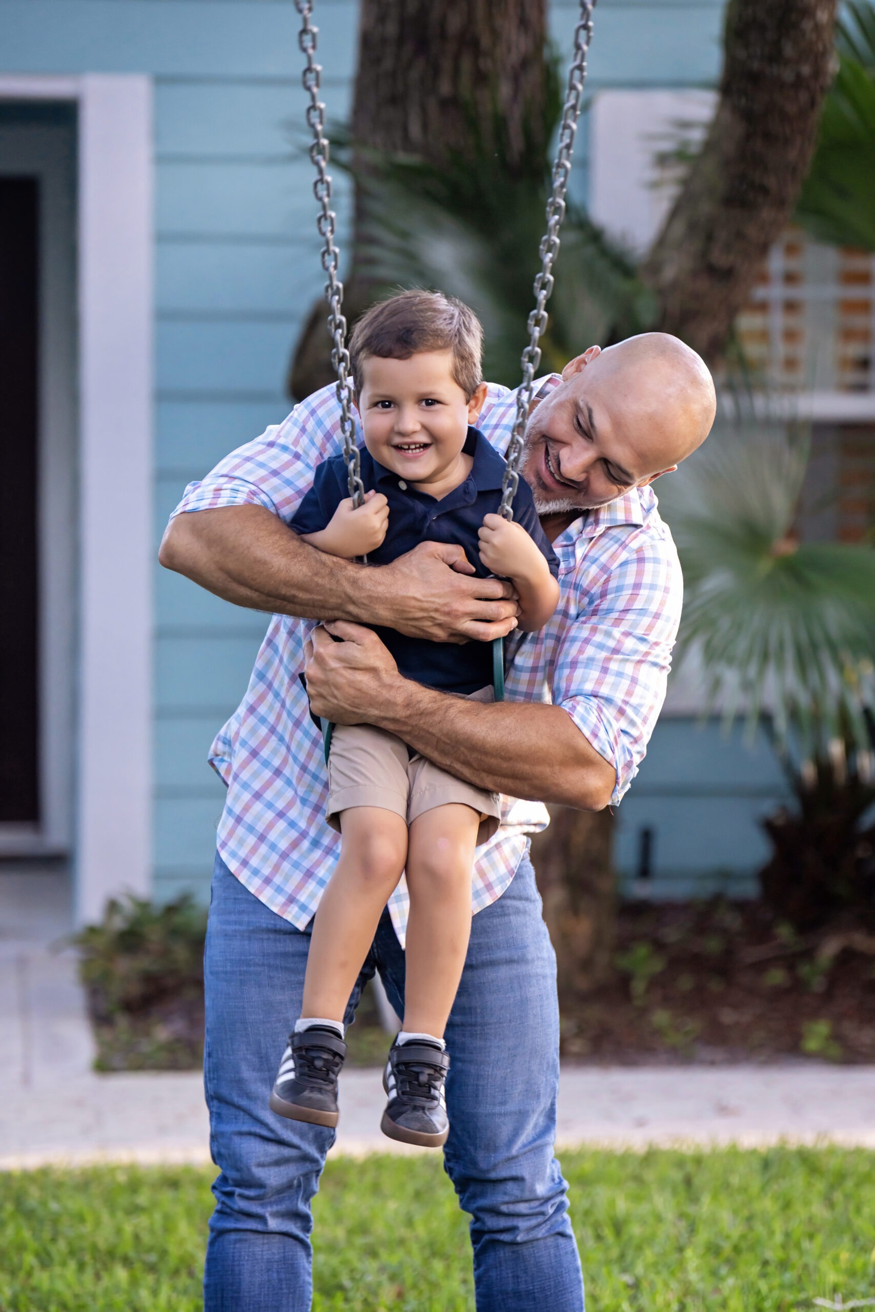 ather and son playing together on a swing during a family photo session in Juno Beach, Florida, captured by David Scarola Photography — a master portrait artist specializing in authentic family moments filled with laughter, love, and connection.