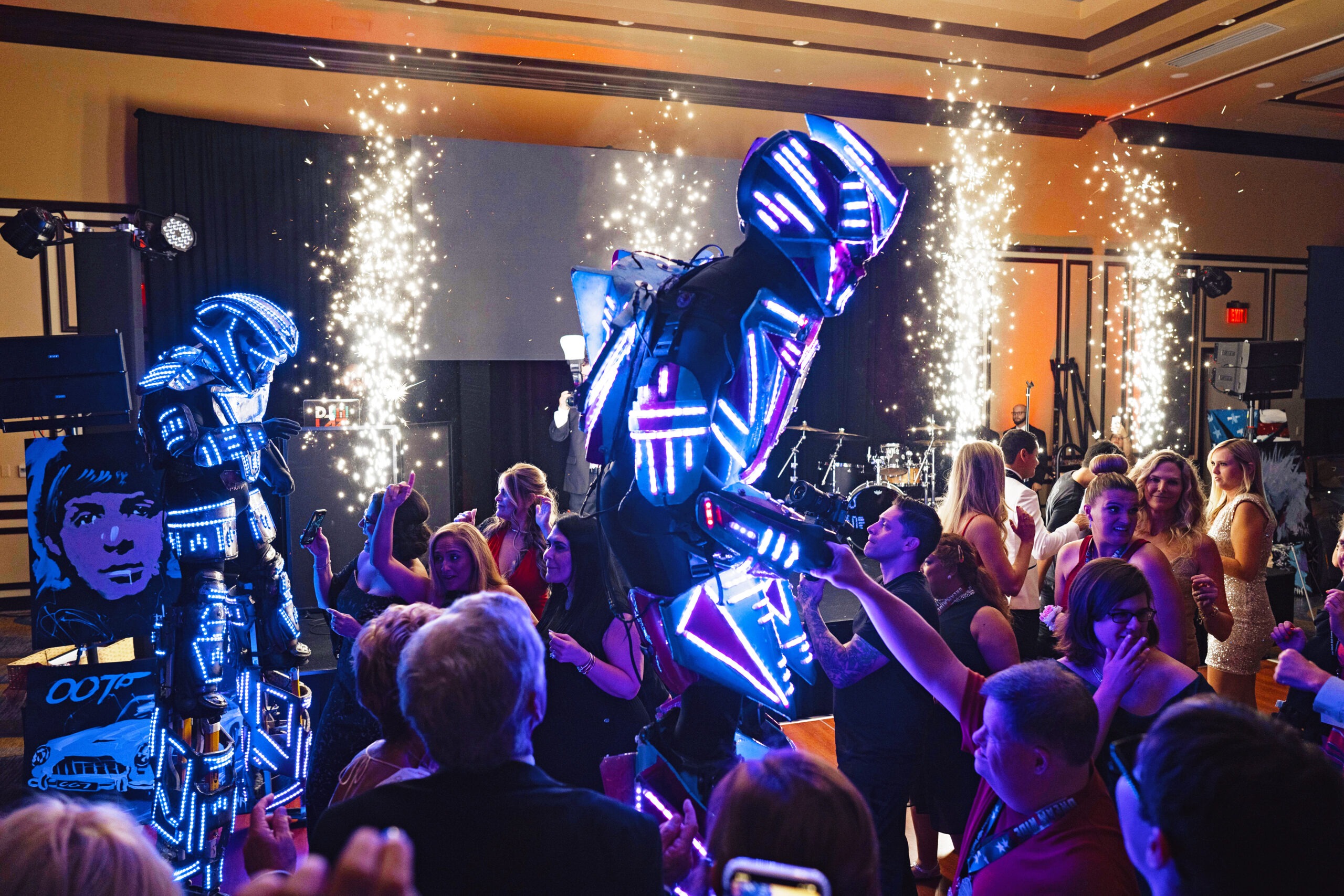 LED robot performers light up the dance floor at the Dream Ride “Cars and Cocktails” Gala in the grand ballroom at PGA National, Palm Beach. Blue and magenta light suits and indoor pyrotechnics illuminate the luxury charity event, captured by master photographer David Scarola for Dream Ride Worldwide Events.Dream Ride Gala, PGA National events, Palm Beach luxury photography, David Scarola Photography, high-end event photographer, gala ballroom photography, LED performers, Transformers on dance floor, global event photography, corporate event photographer Palm Beach, charity gala photos, Cars and Cocktails, worldwide luxury events, Palm Beach photographer.