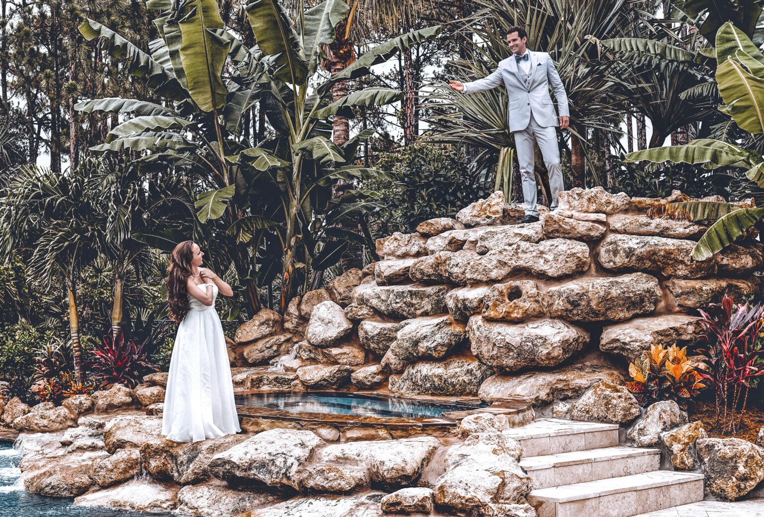 Bride and groom share a beautiful moment beside the cascading rock pool at Old Palm Country Club in Palm Beach Gardens, Florida. Captured by David Scarola Photography, this fine-art wedding portrait radiates elegance, warmth, and tropical sophistication — blending the lush beauty of palm trees, natural stone, and pure emotion.