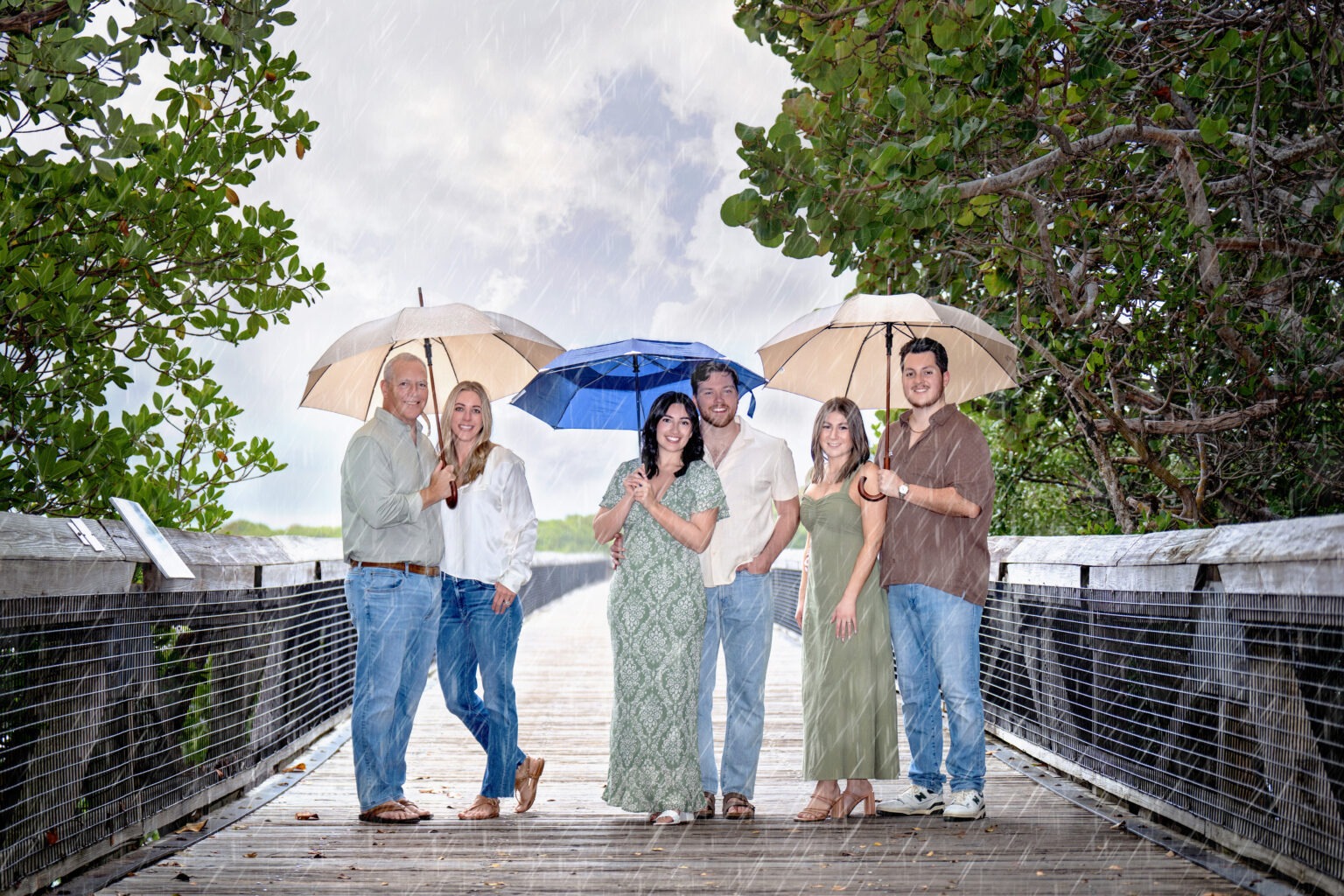 Family portrait at John D. MacArthur State Park on Singer Island, photographed by David Scarola Photography. A joyful family moment captured in the rain, under umbrellas, blending love, laughter, and artistic portraiture. Best family photographer in Palm Beach and Jupiter, South Florida family photo sessions.