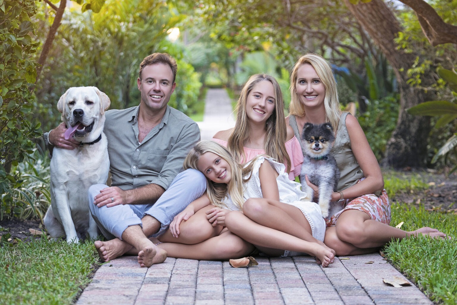 Tony and Devon Julian with their two daughters and dogs share a warm, barefoot moment along the brick path leading to the beach at Jupiter Inlet Colony on Jupiter Island. Captured at sunset, this radiant family portrait glows with natural light, lush greenery, and the relaxed coastal beauty of Palm Beach’s most sought-after photography destination.family photographer Jupiter Island, best family photographer Florida, Jupiter Inlet Colony portraits, Palm Beach family photography, fine art family portraits Jupiter FL, coastal family photography Palm Beach County, professional portrait photographer Jupiter Florida, annual family photo sessions Palm Beach, luxury lifestyle family photographer Florida, top portrait artist Jupiter Island, family portraits with dogs Jupiter FL, Jupiter Island beach photographer, David Scarola Photography family sessions, Florida sunset photography, Palm Beach’s most sought-after photographer