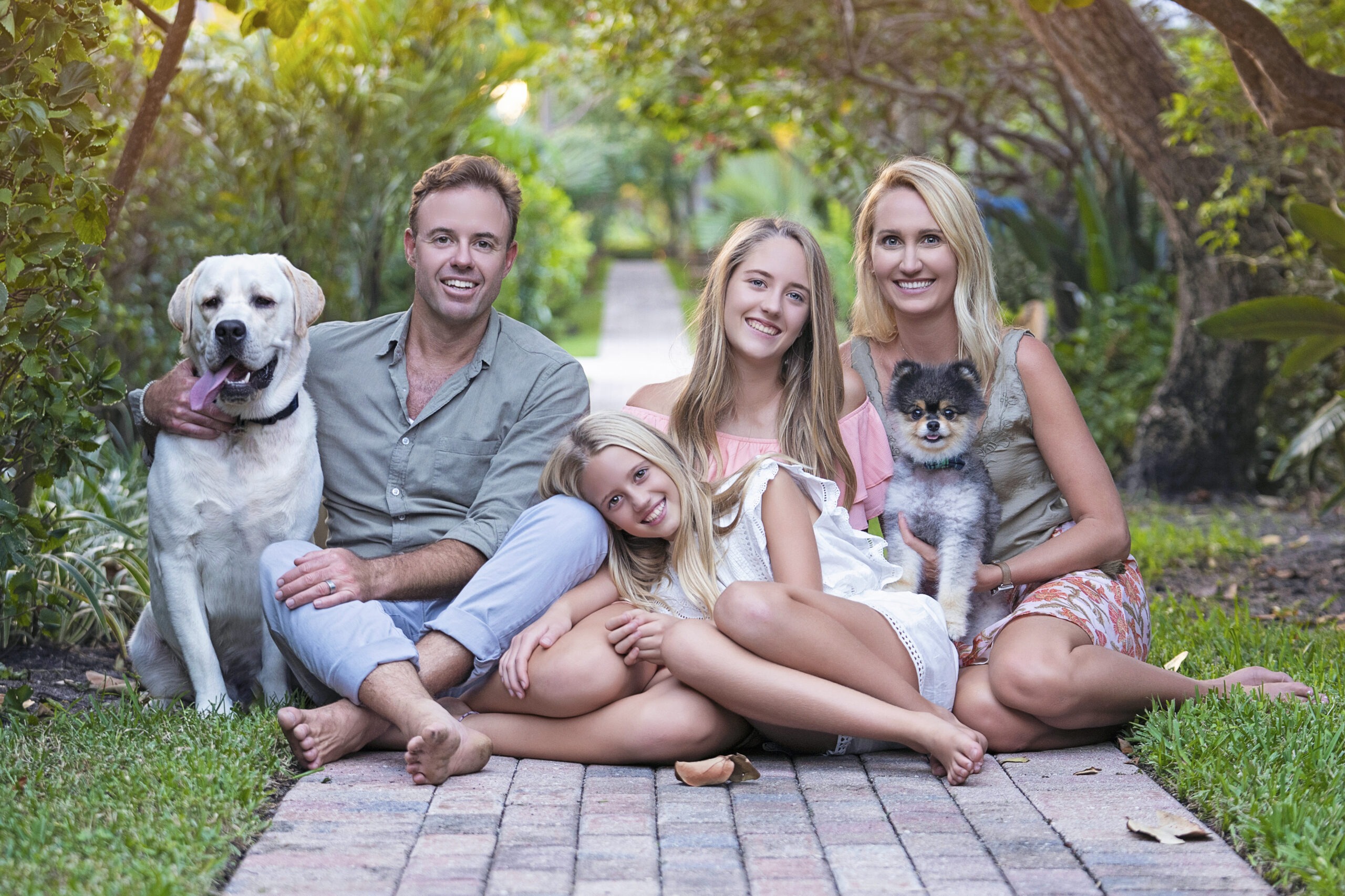 Tony and Devon Julian with their two daughters and dogs share a warm, barefoot moment along the brick path leading to the beach at Jupiter Inlet Colony on Jupiter Island. Captured at sunset, this radiant family portrait glows with natural light, lush greenery, and the relaxed coastal beauty of Palm Beach’s most sought-after photography destination.family photographer Jupiter Island, best family photographer Florida, Jupiter Inlet Colony portraits, Palm Beach family photography, fine art family portraits Jupiter FL, coastal family photography Palm Beach County, professional portrait photographer Jupiter Florida, annual family photo sessions Palm Beach, luxury lifestyle family photographer Florida, top portrait artist Jupiter Island, family portraits with dogs Jupiter FL, Jupiter Island beach photographer, David Scarola Photography family sessions, Florida sunset photography, Palm Beach’s most sought-after photographer