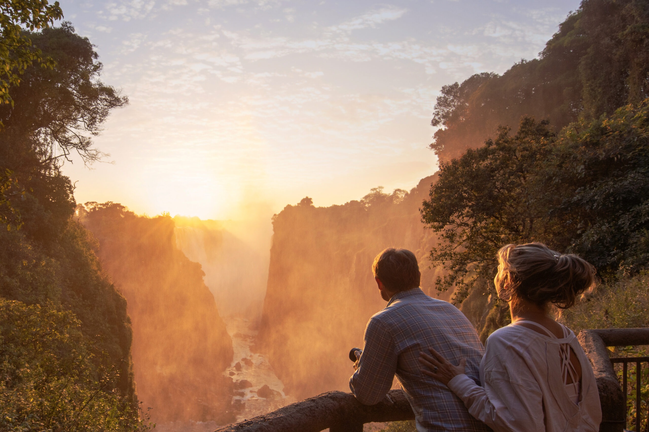 A couple enjoys a peaceful sunrise overlooking Victoria Falls in Zimbabwe, surrounded by golden mist and the roar of cascading water — photographed by David Scarola during the International Academy of Trial Lawyers global adventure.