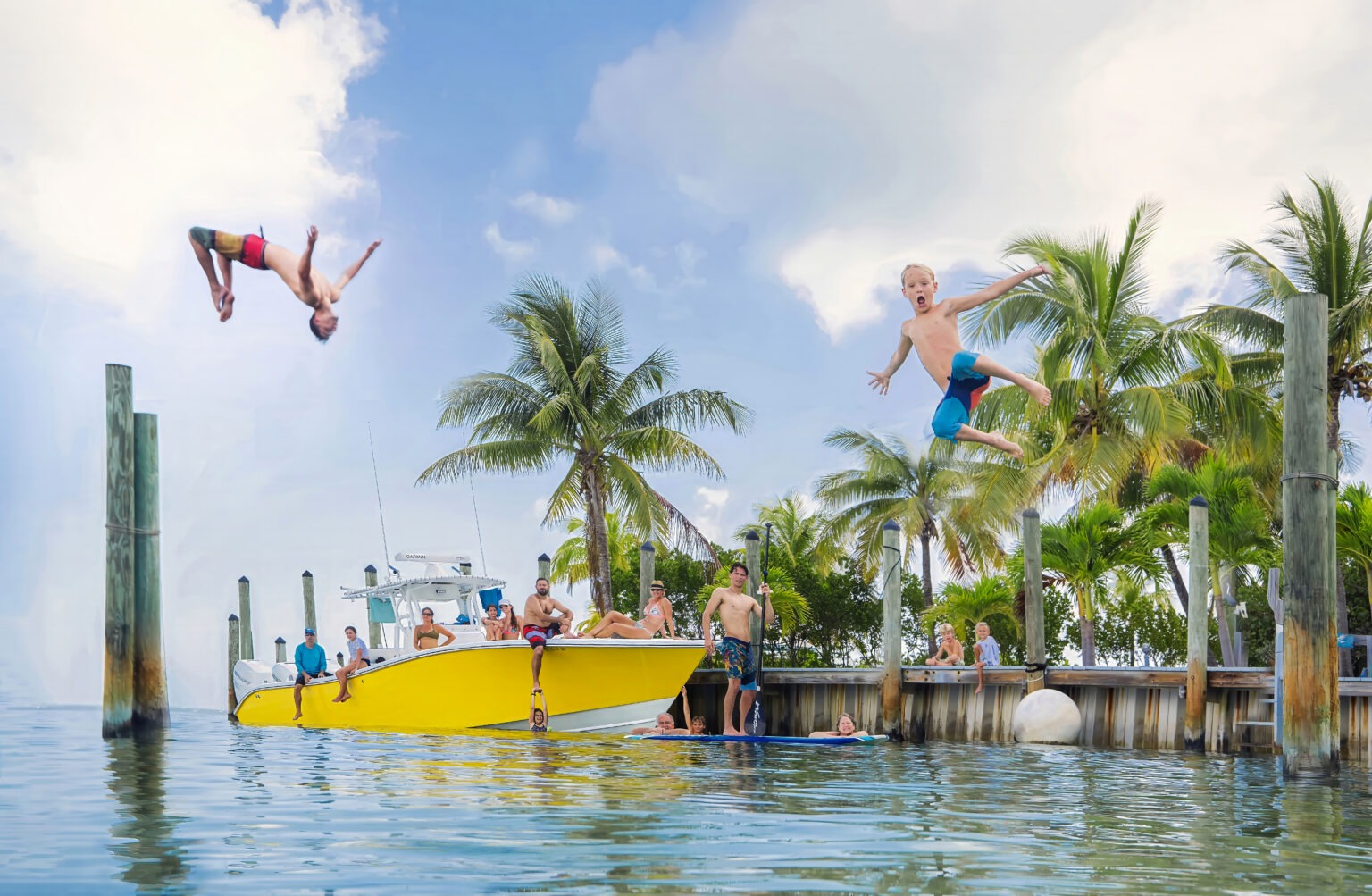 A family vacationing in the bahamas enjoying a bright and happy morning together getting ready for a family boating day gathered playfully and gleefully for a posed family portrait with their family friend and traveling portrait artist, who they hired to join them for 2 days in the bahamas to capture portraits of their family adventure.