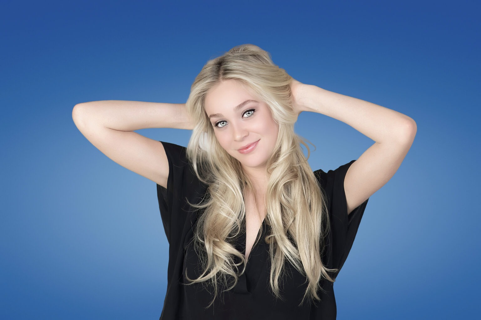 Professional studio headshot of a young woman with long blonde hair wearing a black blouse, posing confidently against a blue background — ideal for LinkedIn, online profiles, and professional branding.professional headshot, young professional portrait, LinkedIn headshot, corporate photography Palm Beach, business headshots Florida, modern portrait photographer, professional branding photography, Jupiter Island, West Palm Beach, Miami, Key Biscayne, online profile photography, studio headshots South Florida, David Scarola Photography.