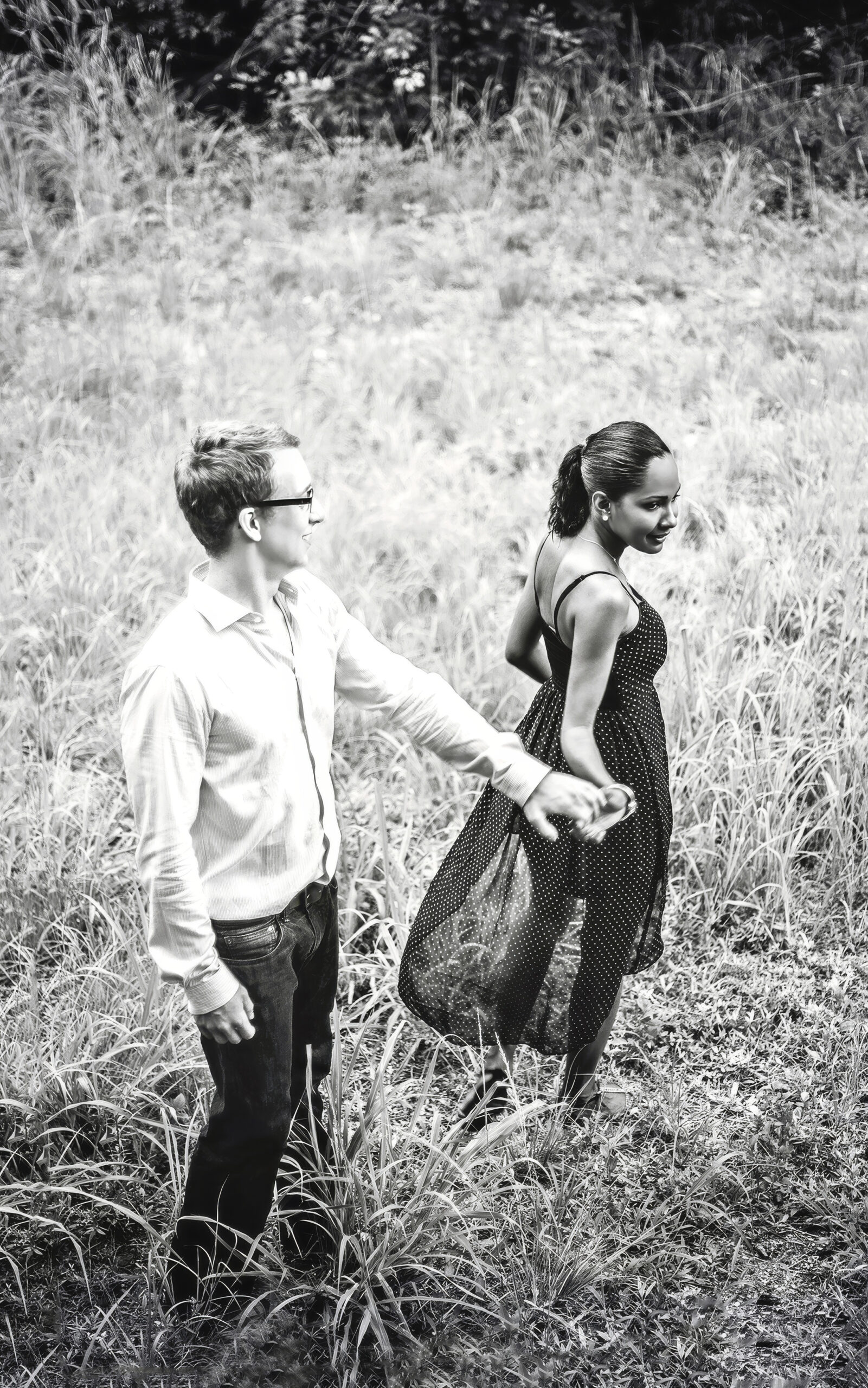 Engaged couple walking hand in hand through a sunlit coastal field by the beach on Jupiter Island, Florida — captured in timeless black and white. The bride-to-be’s dress flows softly in the breeze as their connection radiates through the frame, photographed with emotion and artistry by David Scarola, Florida’s best engagement and fine-art wedding photographer renowned for cinematic storytelling and soulful portraiture.