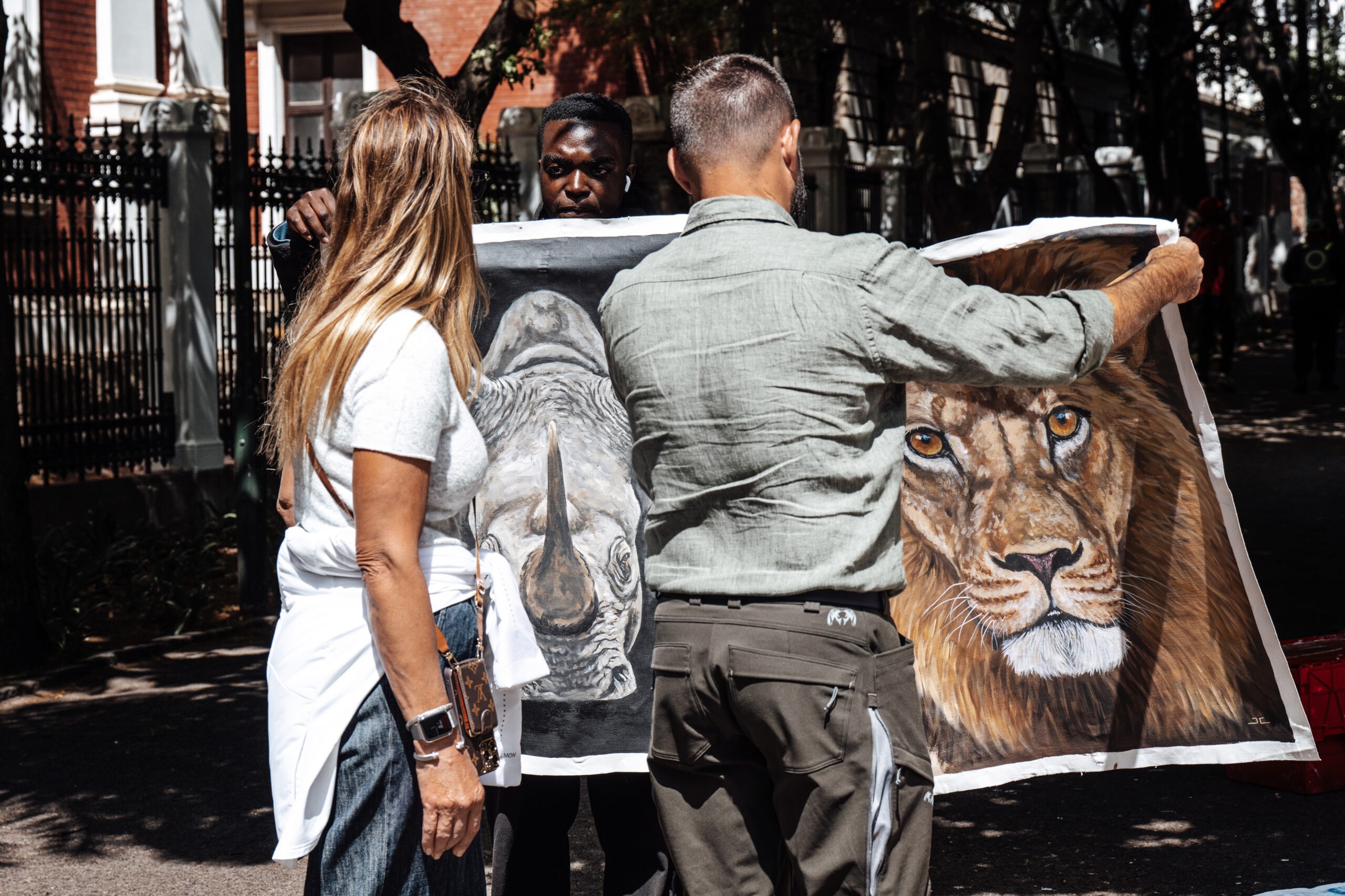 Travelers exploring a street art market in Cape Town, South Africa, admiring a painting of a lion and a rhinoceros — captured by David Scarola Photography during a day in Cape Town.Cape Town street photography, South Africa travel photographer, David Scarola Photography, African art market, Cape Town cultural photography, luxury travel photographer South Africa, street art in Cape Town, wildlife art photography, day in Cape Town, professional travel photographer, global event photographer, cultural storytelling photography, international destination photography.