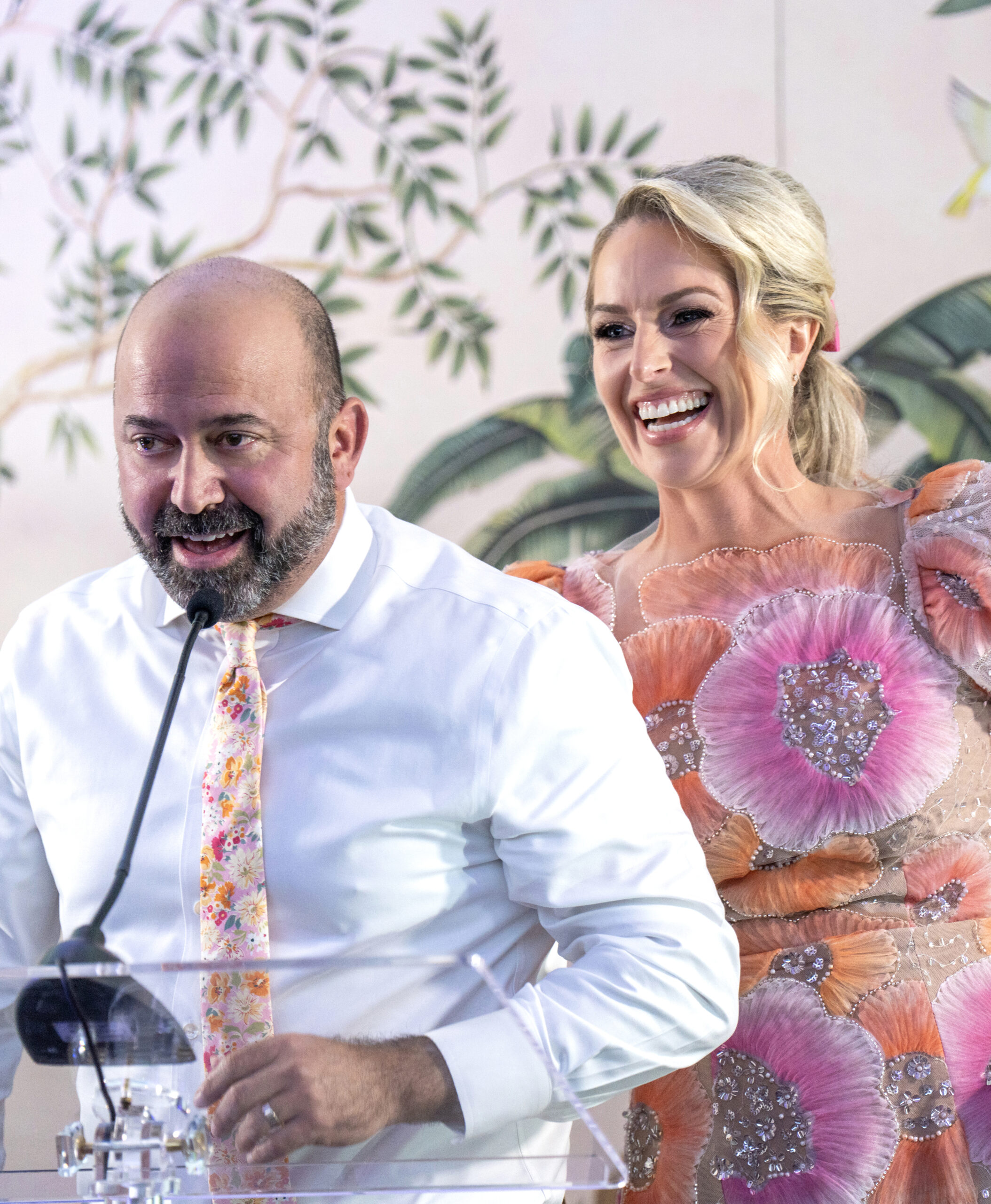 Heather and Steve Laughlin speaking on stage at the Live Like Jake Gala at The Pelican Club in Jupiter Island, Florida. Steve addresses the audience at the podium while Heather, wearing a floral gown, smiles beside him in celebration of the foundation’s mission.Live Like Jake Gala, Heather and Steve Laughlin, Pelican Club Jupiter Island, Jupiter Island charity gala, Palm Beach event photographer, Florida gala photography, nonprofit event photography, David Scarola Photography, luxury event coverage, high-end gala photographer, philanthropy photography, Jupiter Island event coverage, Palm Beach social events.