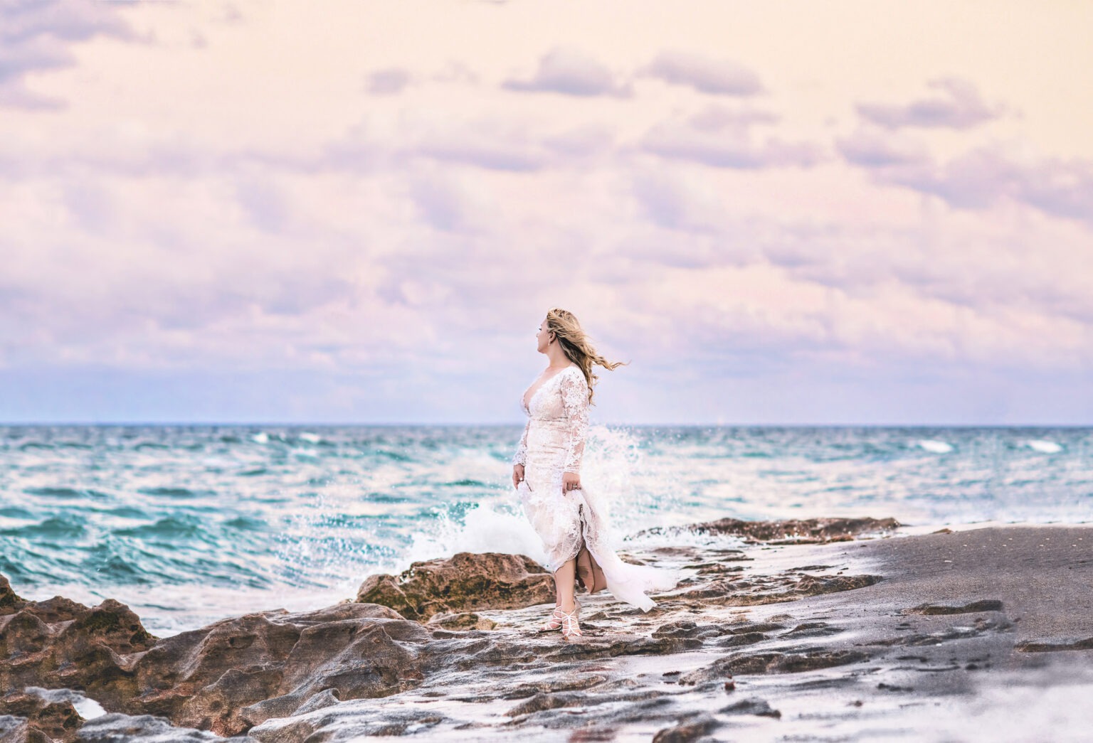 Bride standing on the coral shore of Jupiter Island as waves crash and sunset light paints the sky in pastels — her lace gown catching the ocean breeze. Captured in ethereal perfection by David Scarola, the visionary fine-art wedding photographer whose lens turns love, light, and landscape into poetry.