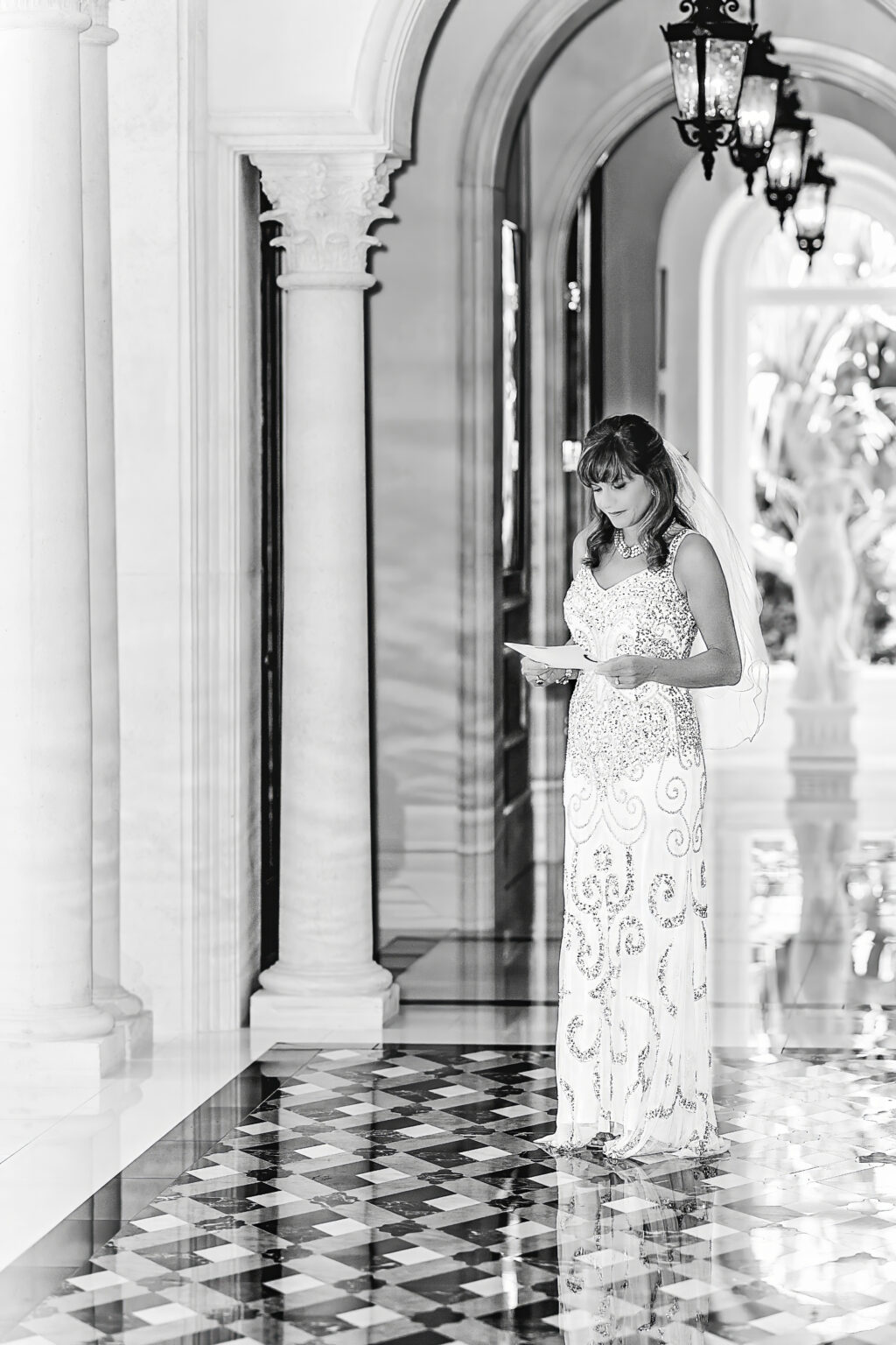 Bride standing elegantly in the marble corridor of Old Palm Country Club in North Palm Beach, Florida — a premier golf and tennis community and one of Palm Beach County’s most luxurious wedding venues. She reads a heartfelt note before the ceremony, her gown shimmering under the light and reflecting on the polished black-and-white floor — captured in timeless fine-art style by David Scarola, Florida’s best wedding photographer, acclaimed for his luminous, emotive, and magazine-worthy wedding portraiture.
