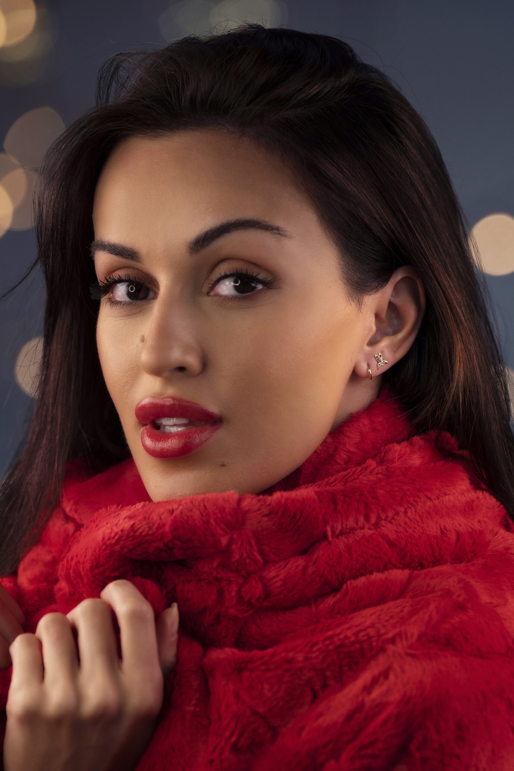 Close-up fashion and lifestyle portrait of a model wearing fine jewelry earrings by FreshTrends LLC, photographed in-studio by David Scarola, an acclaimed commercial, fashion, and lifestyle photographer based in Jupiter and Palm Beach, Florida. The model is wrapped in a vibrant red fur shawl with bold red lipstick, creating a luxurious, high-end aesthetic that highlights both the elegance of the jewelry and the refined artistry of Scarola’s studio lighting and composition.David Scarola Photography, FreshTrends LLC, jewelry photographer Florida, product and lifestyle photography, fashion photographer Palm Beach, professional studio photographer Jupiter, commercial jewelry photoshoot, fine art fashion photographer, luxury product photography, e-commerce jewelry imagery, professional portrait photographer Florida, FreshTrends jewelry campaign, David Scarola Studio photoshoot, lifestyle brand photographer Palm Beach County, high-end fashion portrait photography, beauty and accessories photographer, luxury brand photographer Florida, top commercial photographer USA, creative advertising photography, fine jewelry photography.