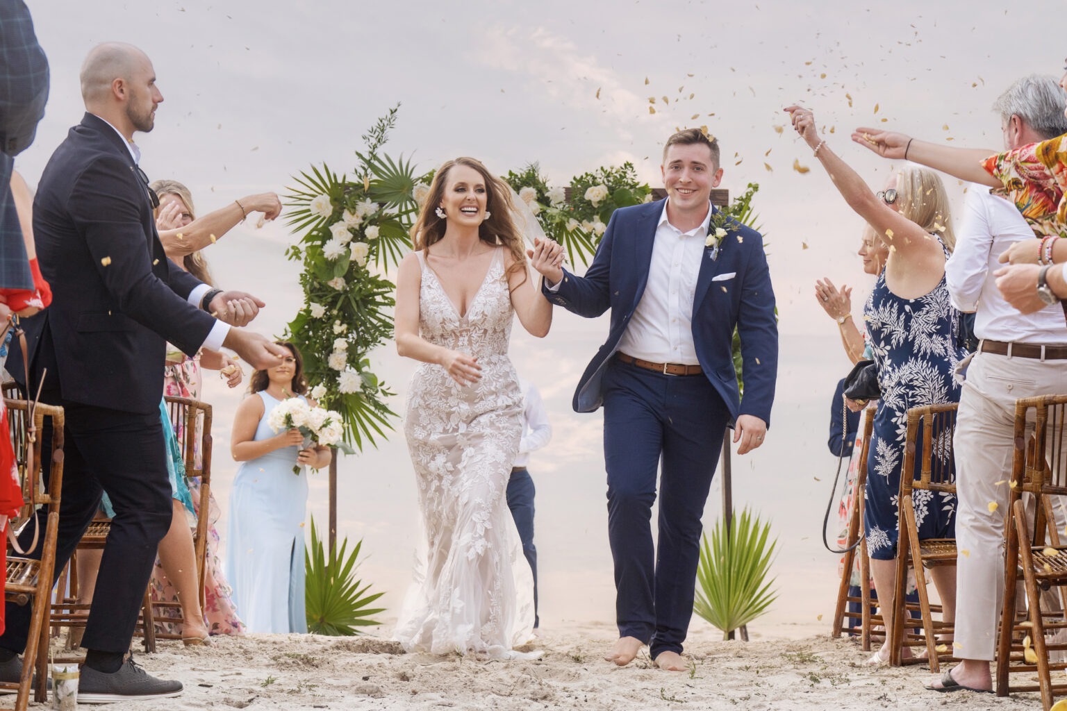 Bride and groom walk hand-in-hand down a white sand beach in Eleuthera, The Bahamas, just after their oceanfront wedding ceremony. Captured by world-class destination photographer David Scarola, this image blends romance, artistry, and natural island light as the couple moves toward a glowing pastel sunset reflecting on the calm Caribbean waters.