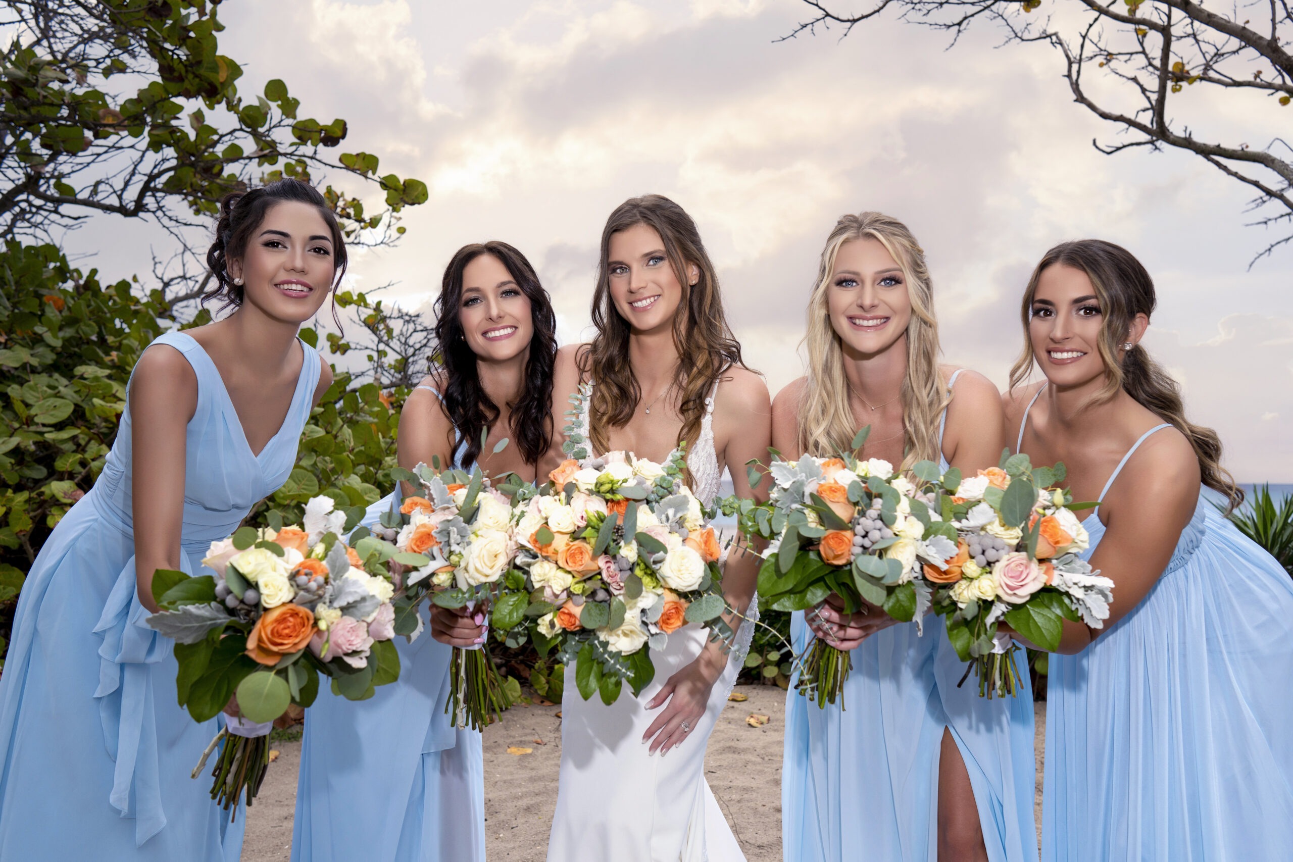 Bride surrounded by her radiant bridesmaids in soft sky-blue gowns, each holding lush floral bouquets of cream, coral, and sage — framed by Jupiter Beach’s golden light and ocean breeze. Captured in stunning fine-art fashion by David Scarola, Florida’s premier luxury wedding photographer celebrated for his cinematic lighting, masterful color balance, and ability to blend emotion, beauty, and artistry into every frame.