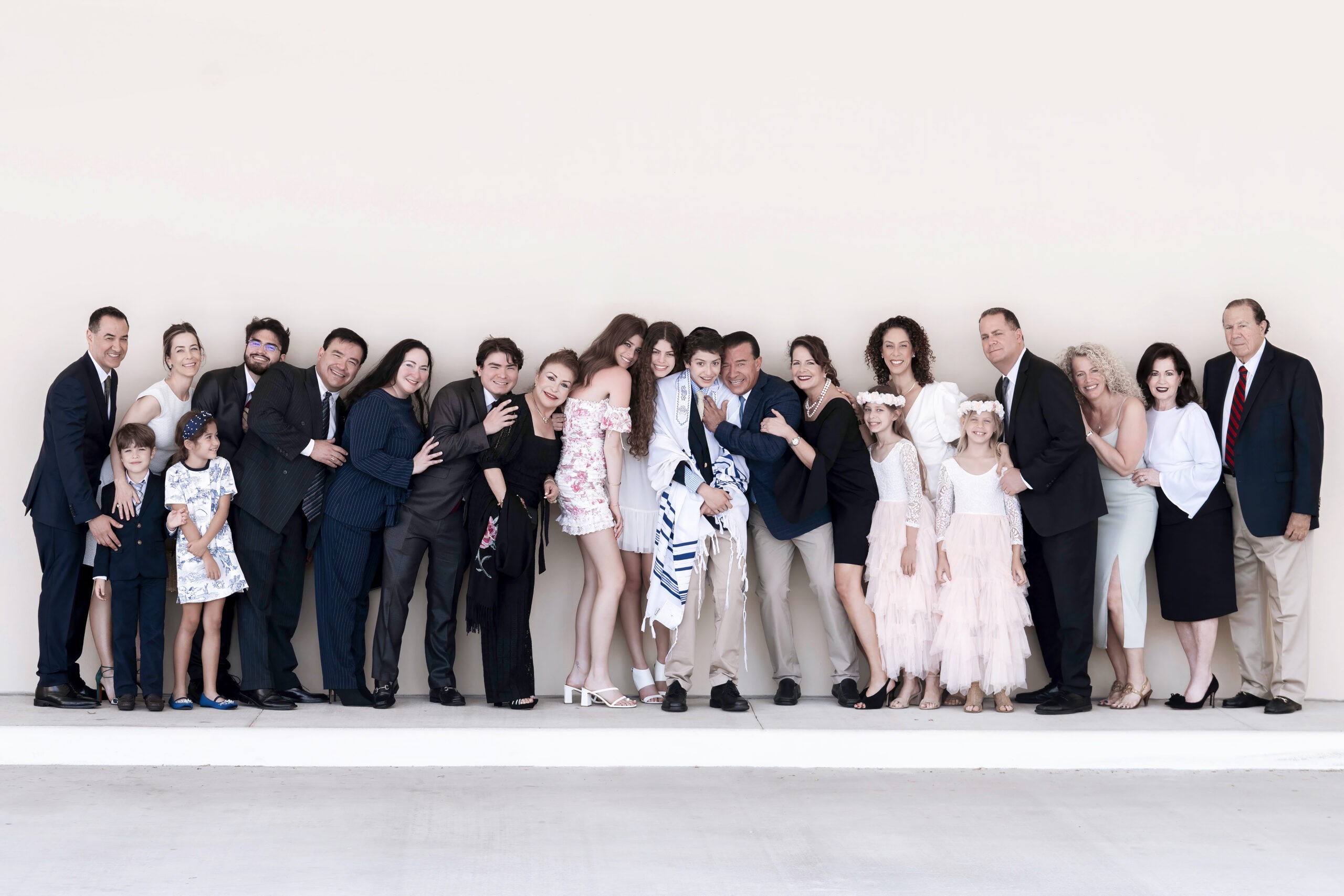 A large Palm Beach family gathers in elegant attire for Aiden’s Bar Mitzvah celebration, smiling and leaning together in joyful unity. The group includes men, women, and children dressed formally, standing against a clean neutral background for a refined, modern family portrait.Aiden’s Bar Mitzvah Palm Beach, Jewish family photography, luxury event photographer Florida, professional Bar Mitzvah photography, Palm Beach family portrait, David Scarola Photography, milestone celebrations, private event photographer, high-end portrait photography, worldwide event photography, elegant family photography, Jewish traditions photographer.