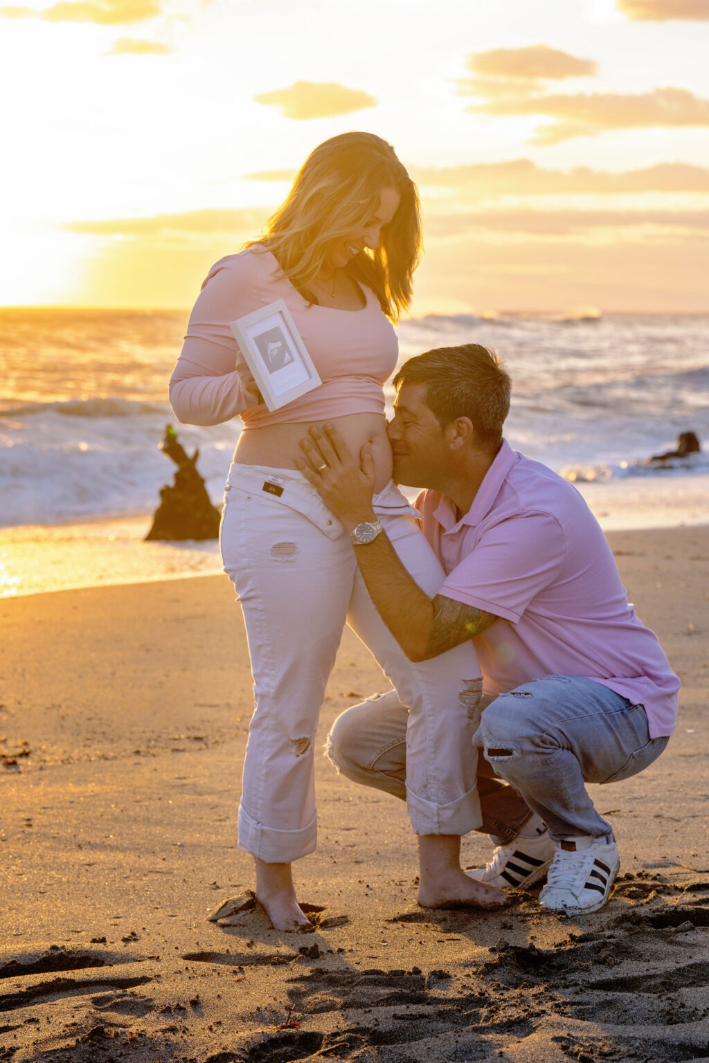 Emotional baby announcement photo session on Jupiter Island, captured by David Scarola Photography. Expectant parents celebrate new life during a golden sunset on the beach, holding an ultrasound and sharing a kiss on the mother’s belly. Heartfelt maternity photography in Jupiter, Florida, blending love, light, and family.