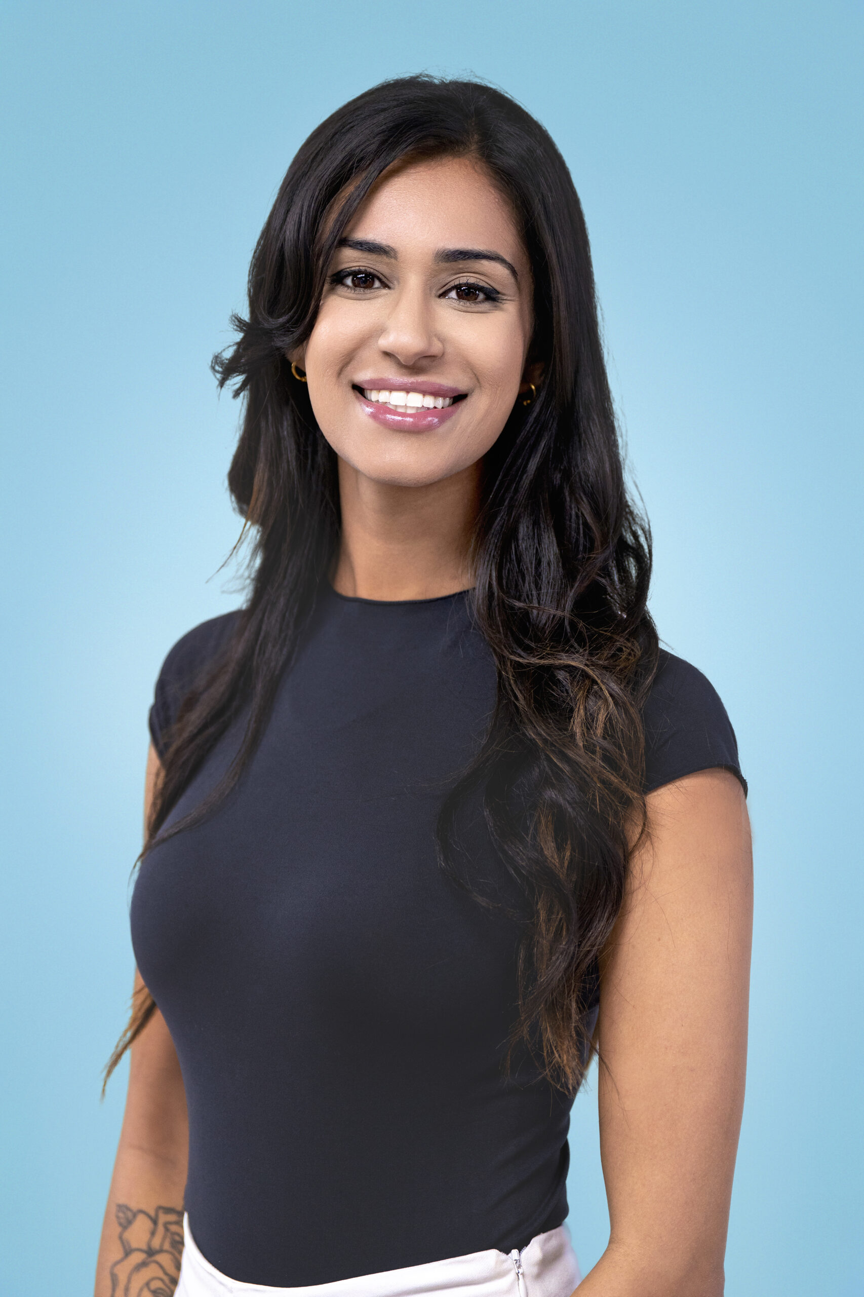Studio headshot of a young professional woman with long dark hair smiling confidently against a light blue background. Professional branding photography by David Scarola Photography, Palm Beach & South Florida.studio headshot Palm Beach, young professional portrait Florida, personal branding photography South Florida, corporate headshot Miami, headshot photographer Jupiter Island, professional portrait Palm Beach County, business headshots South Florida, David Scarola Photography, modern branding portrait Florida, LinkedIn profile photographer Palm Beach.
