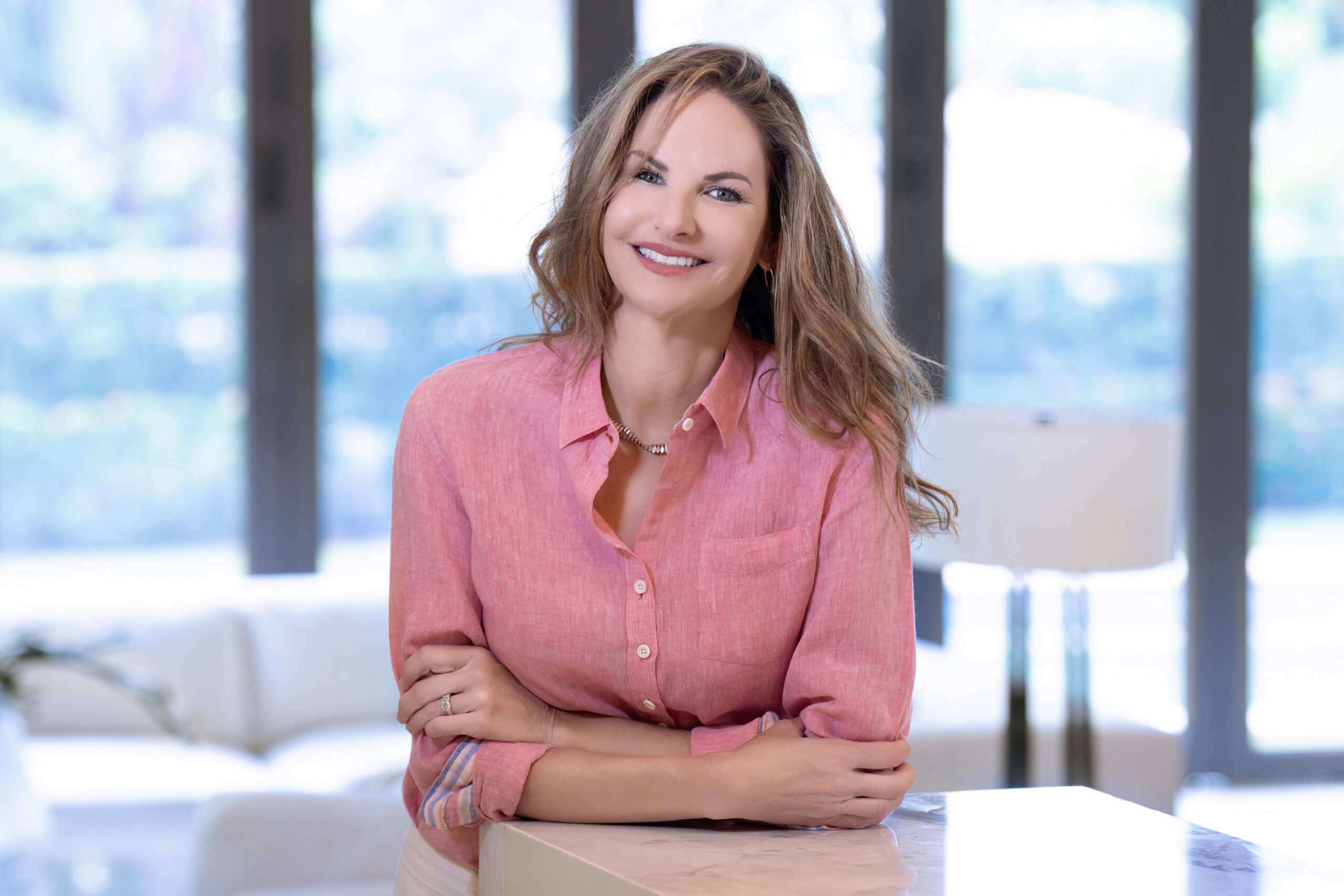 Professional headshot of a smiling interior designer wearing a pink blouse in a bright, modern home setting. Captured by David Scarola Photography, Palm Beach and Jupiter Island, Florida.interior designer headshot Palm Beach, professional headshot Jupiter Island, personal branding photography South Florida, lifestyle portrait photographer Palm Beach, business portrait Miami, creative professional photography Florida, interior design branding photos, best headshot photographer Palm Beach County, David Scarola Photography, modern natural light headshots Florida.