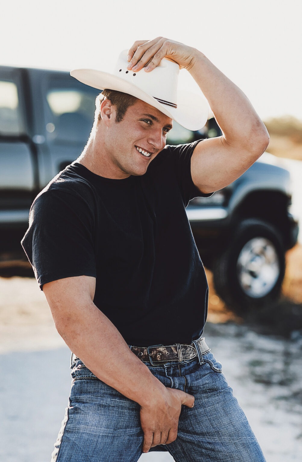 A confident cowboy in jeans and a black T-shirt adjusts his white hat with a playful smile beside a rugged Chevy truck under the Florida sun. Captured by David Scarola Photography, this image embodies masculine energy, Florida country style, and the bold spirit of modern Americana.David Scarola Photography, Florida cowboy portrait, Chevy truck lifestyle shoot, country fashion editorial, Palm Beach country style, Jupiter Florida photographer, masculine brand campaign, Florida western fashion, Chevy brand ambassador photography, lifestyle influencer shoot, all-American fashion photography, countryman editorial, Palm Beach Illustrated photographer, Jupiter Magazine fashion, South Florida commercial portraiture, rugged male model campaign, modern cowboy aesthetic, brand photography Florida, editorial portrait art, David Scarola fine art commercial.