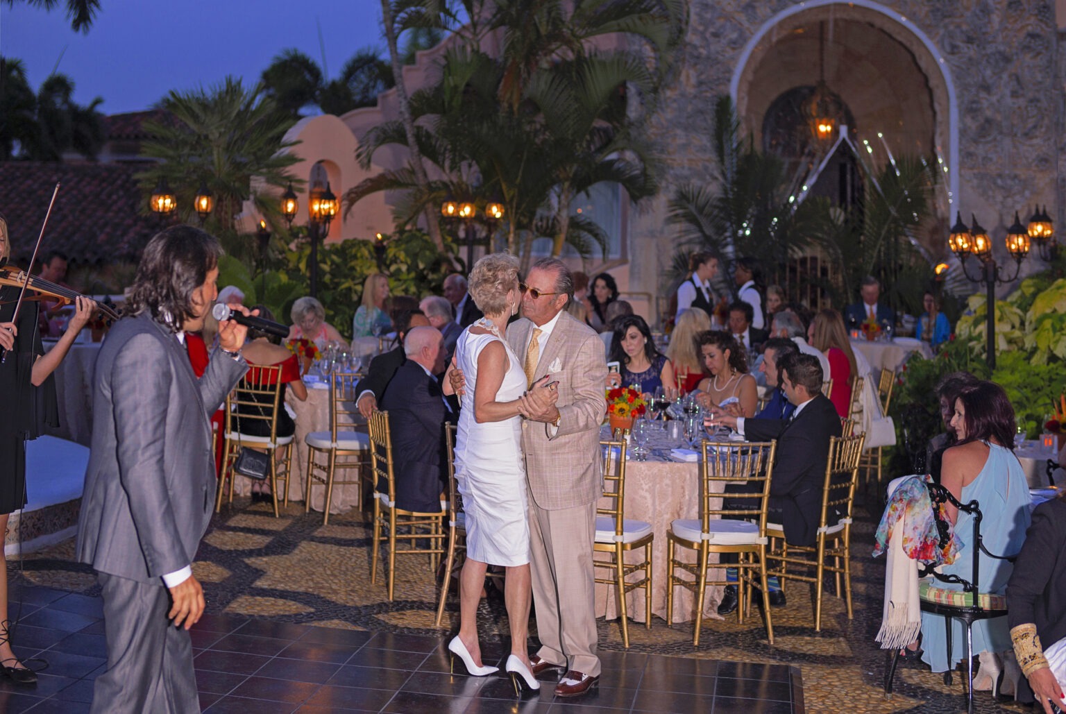An elegant couple dances under the evening sky at Mar-a-Lago, surrounded by guests enjoying a private opera dinner performance by Franco Corso. The scene radiates luxury, intimacy, and Old-World glamour, with golden light, live musicians, and refined décor creating the perfect backdrop for an unforgettable night of art and celebration.
