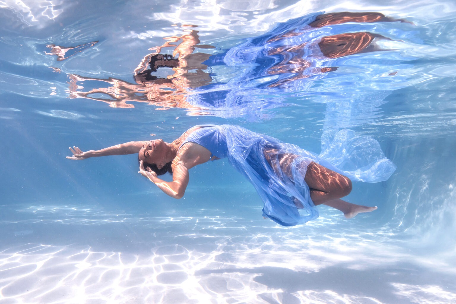 Underwater fashion photography of a model in a flowing blue gown, captured at the Ritz-Carlton in Key Biscayne for The Webster Miami boutique campaign. Elegant, weightless movement illuminated by sunlight beneath crystal-clear water, photographed by master fashion photographer David Scarola.The Webster Miami fashion shoot, Ritz-Carlton Key Biscayne photography, underwater fashion photographer, Miami luxury fashion campaign, resort wear photography, couture underwater portrait, David Scarola Photography, luxury lifestyle imagery, underwater fine art, Miami boutique campaign.