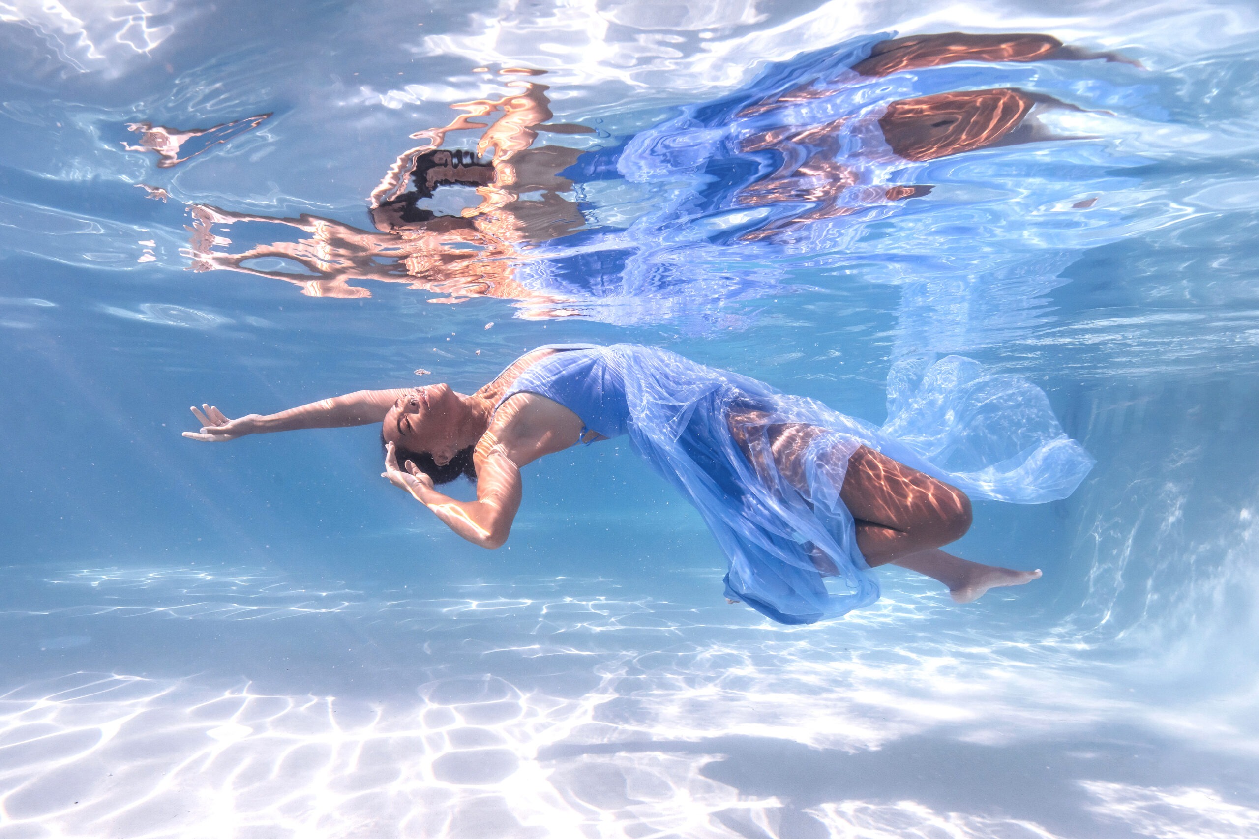 Underwater fashion photography of a model in a flowing blue gown, captured at the Ritz-Carlton in Key Biscayne for The Webster Miami boutique campaign. Elegant, weightless movement illuminated by sunlight beneath crystal-clear water, photographed by master fashion photographer David Scarola.The Webster Miami fashion shoot, Ritz-Carlton Key Biscayne photography, underwater fashion photographer, Miami luxury fashion campaign, resort wear photography, couture underwater portrait, David Scarola Photography, luxury lifestyle imagery, underwater fine art, Miami boutique campaign.