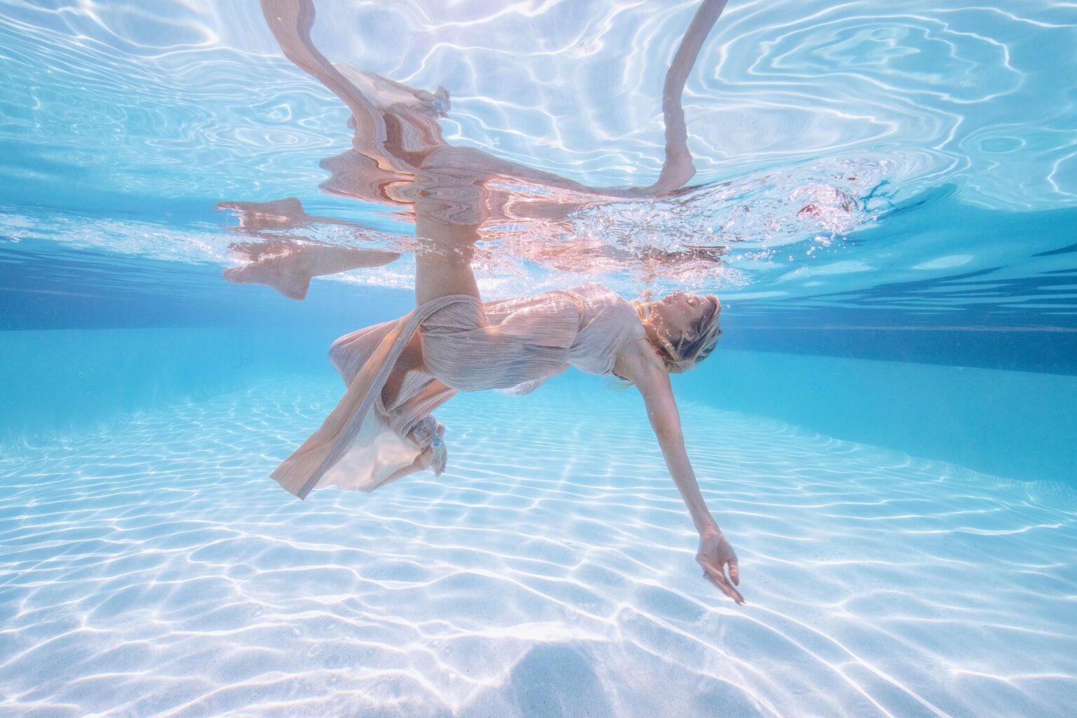 Underwater fashion photography of a model in a flowing champagne gown, gracefully arching in crystal-clear turquoise water. Captured by renowned photographer David Scarola, this ethereal fine-art image blends elegance, movement, and light for luxury resort campaigns and high-end fashion editorials.underwater fashion photography, luxury resort editorial, South Florida fine art photographer, underwater elegance, fashion marketing photography, Palm Beach creative branding, underwater couture, resort lifestyle photographer, professional commercial photographer Florida.