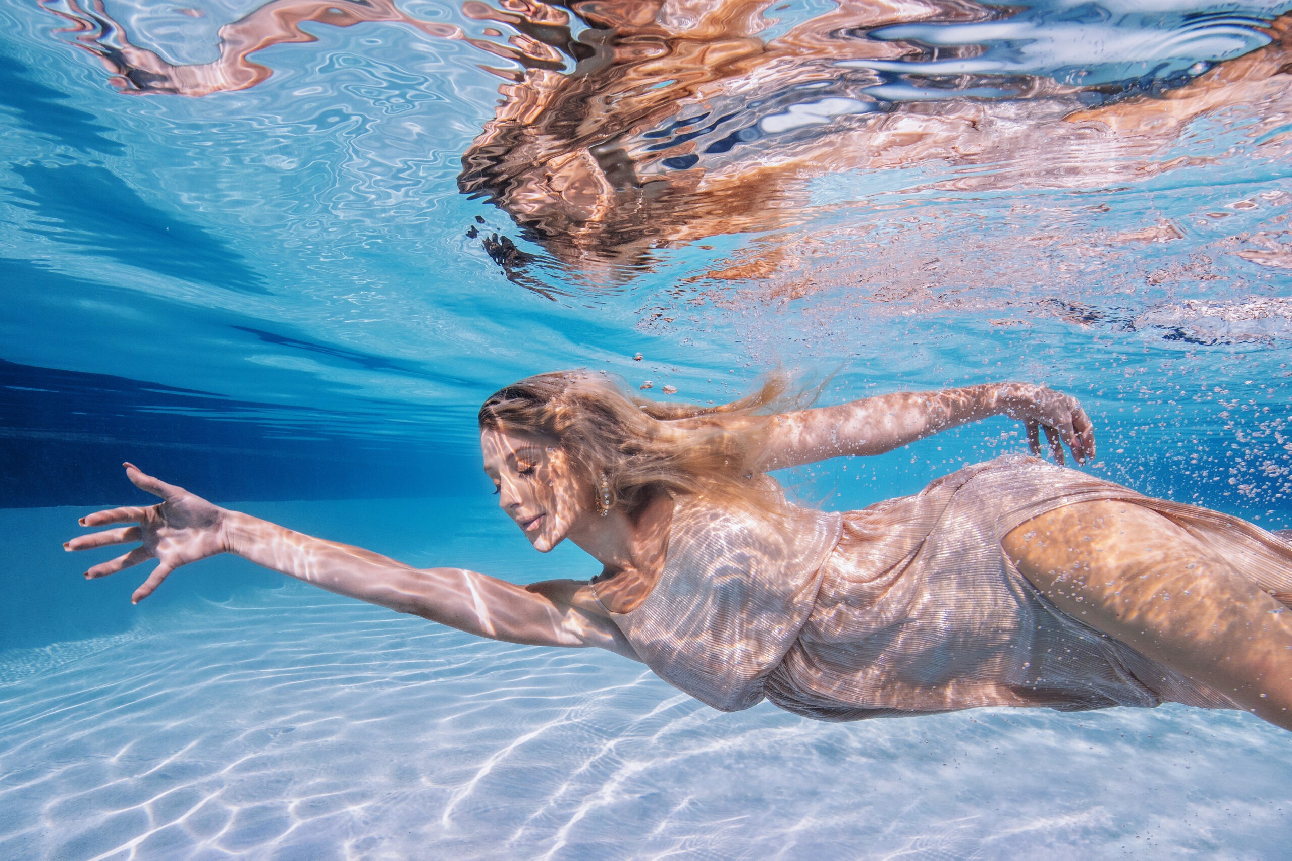 Underwater fashion photography at The Ritz-Carlton Fort Lauderdale featuring a model in a flowing gold designer gown by The Webster Miami, photographed by David Scarola. Captured mid-motion beneath crystal blue water, this image highlights luxury resort fashion, artistic elegance, and fine art underwater portraiture.David Scarola Photography, underwater fashion photography, luxury resort fashion shoot, The Ritz-Carlton Fort Lauderdale, The Webster Miami campaign, fine art underwater portrait, South Florida fashion photographer, creative underwater photoshoot, Palm Beach luxury photographer, high-end editorial photography, professional commercial photography Jupiter Florida, underwater model photography.