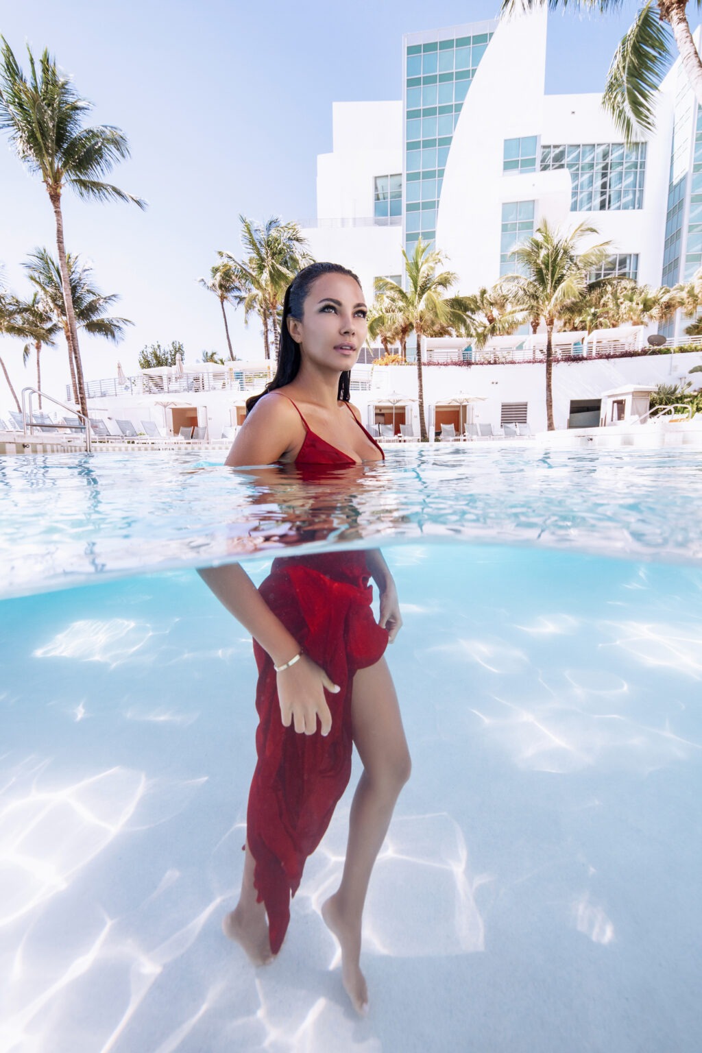 Luxury fashion and lifestyle photo shoot at The Ritz-Carlton Fort Lauderdale featuring a model in a red designer dress by The Webster Miami, photographed poolside by award-winning Palm Beach photographer David Scarola. Creative underwater portrait captures elegance, sunlight, and architectural luxury.David Scarola Photography, The Ritz-Carlton Fort Lauderdale fashion shoot, The Webster Miami campaign, luxury fashion photography Florida, creative underwater portraiture, Palm Beach lifestyle photographer, Fort Lauderdale commercial photography, high-end resort photo shoot, professional photographer South Florida, underwater fashion photography Miami.
