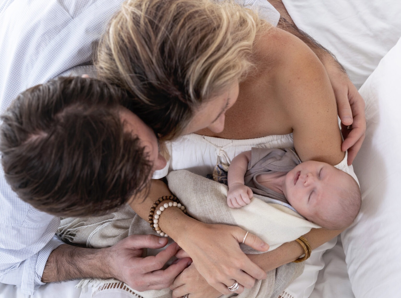 Newborn photography session capturing a tender family moment — baby peacefully asleep in the loving arms of mom and dad. Natural light lifestyle portrait by David Scarola Photography, renowned for Palm Beach and Jupiter newborn photography, family portraits, and fine-art lifestyle sessions.