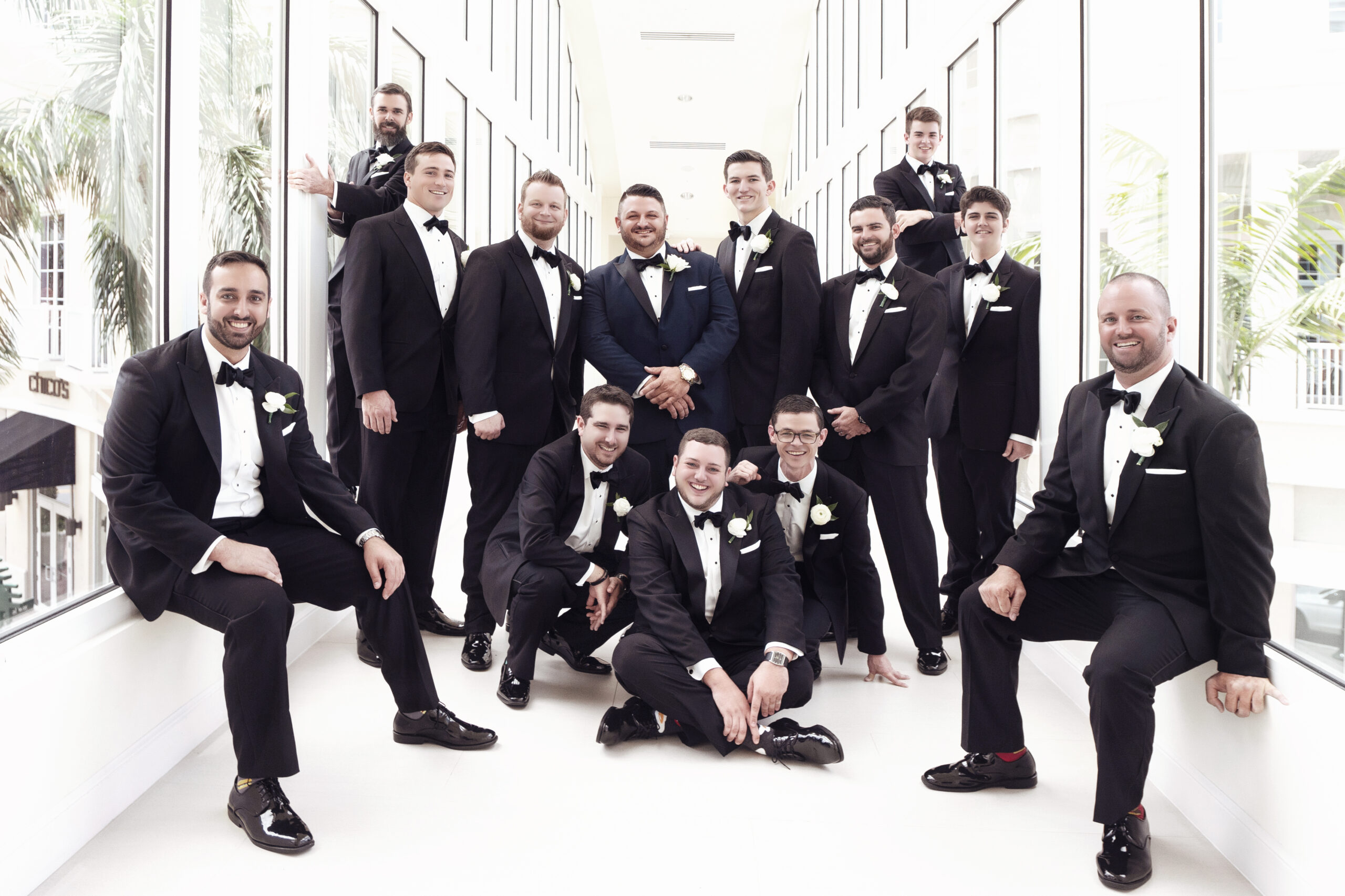 Groom surrounded by his groomsmen at the Wyndham Grand Jupiter on Jupiter Island, Florida. Captured by David Scarola Photography, this dynamic wedding portrait highlights friendship, laughter, and timeless style — a group of sharply dressed men in classic black tuxedos celebrating before the ceremony.
