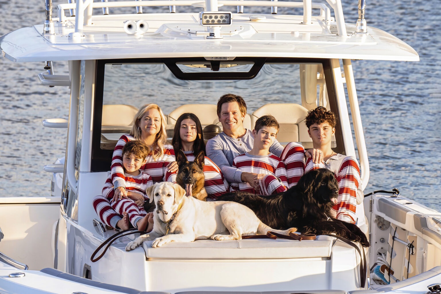 Brian and Tiffany Rooney with their children and family dogs enjoying sunset on their boat during a holiday family portrait session in Jupiter Island, Florida. Everyone is dressed in festive red-and-white pajamas, creating a warm, joyful atmosphere of love and connection. Photographed by David Scarola Photography, master of fine art and lifestyle family photography.