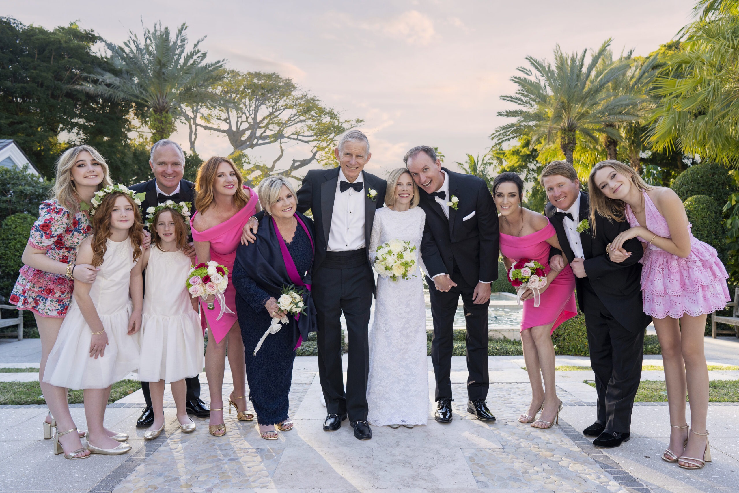 Bride and groom surrounded by their joyful family after the wedding ceremony at The Royal Poinciana Chapel on Palm Beach Island. Captured by David Scarola Photography, Palm Beach’s premier fine-art wedding photographer known for timeless portraiture, natural light mastery, and genuine emotion. The image radiates love, legacy, and connection beneath the tropical palms of Palm Beach, blending elegance with authenticity.