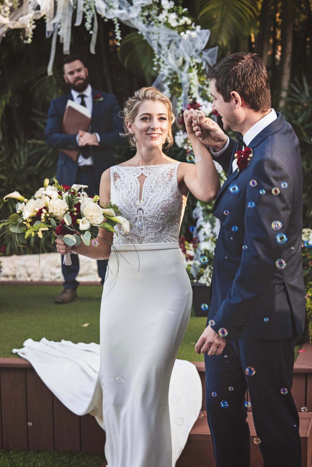 Bride and groom sharing a joyful, elegant moment just after saying “I do” on Palm Beach Island — surrounded by tropical greenery, bubbles floating through the sunlight, and a romantic floral arch. Captured with timeless artistry and refined emotion by David Scarola, Palm Beach’s best wedding photographer and fine-art portrait specialist known for luminous, cinematic, and heart-centered wedding imagery.