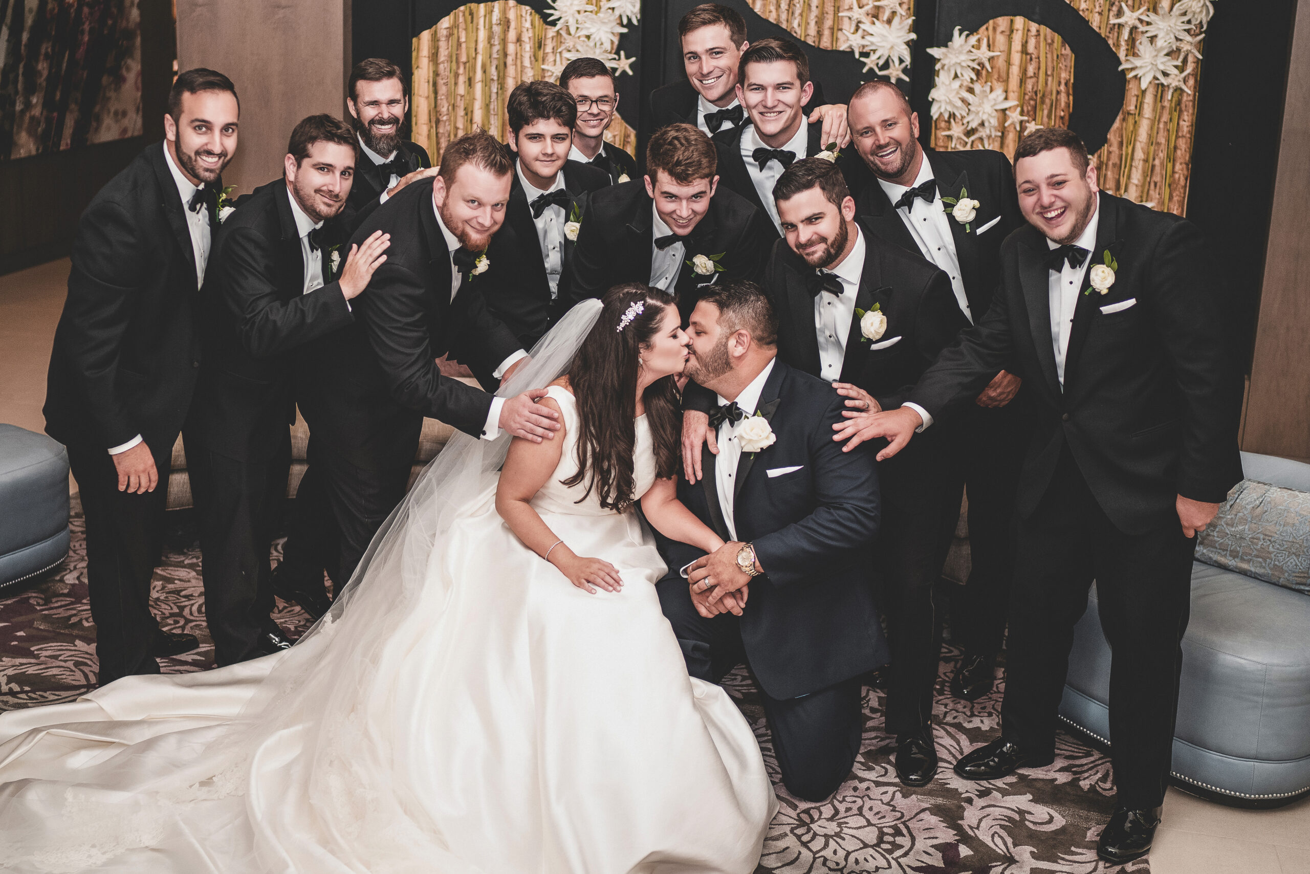Bride and groom share a kiss surrounded by the groomsmen at the Wyndham Grand in Jupiter, Florida — captured by South Florida wedding photographer David Scarola. A joyful, heartfelt wedding moment filled with laughter, brotherhood, and celebration.