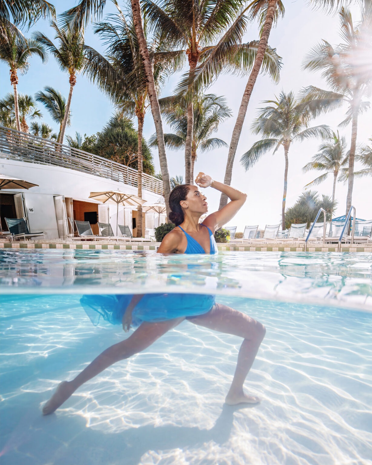 Fashion and lifestyle portrait of an influencer and model posing half above and half below water in a luxury pool in Fort Lauderdale, Florida, photographed by David Scarola, one of the top fashion and lifestyle photographers in Palm Beach, Jupiter, and the United States. Wearing a flowing blue dress beneath tall palm trees and radiant sun, the model strikes a dynamic pose that captures movement, elegance, and confidence — a perfect fusion of fine art fashion and resort lifestyle imagery.David Scarola Photography, Fort Lauderdale fashion photographer, Palm Beach lifestyle photographer, Jupiter Florida photography, underwater fashion photography, resort lifestyle imagery, professional influencer photoshoot, luxury fashion photographer, beach and pool photography, brand image photography, fine art fashion photographer Florida, best lifestyle photographer USA, female model portrait, resort fashion campaign, Scarola style photography, professional branding photoshoot, creative luxury photography, underwater portrait photography, Florida resort photoshoot, fashion and lifestyle photographer Fort Lauderdale.