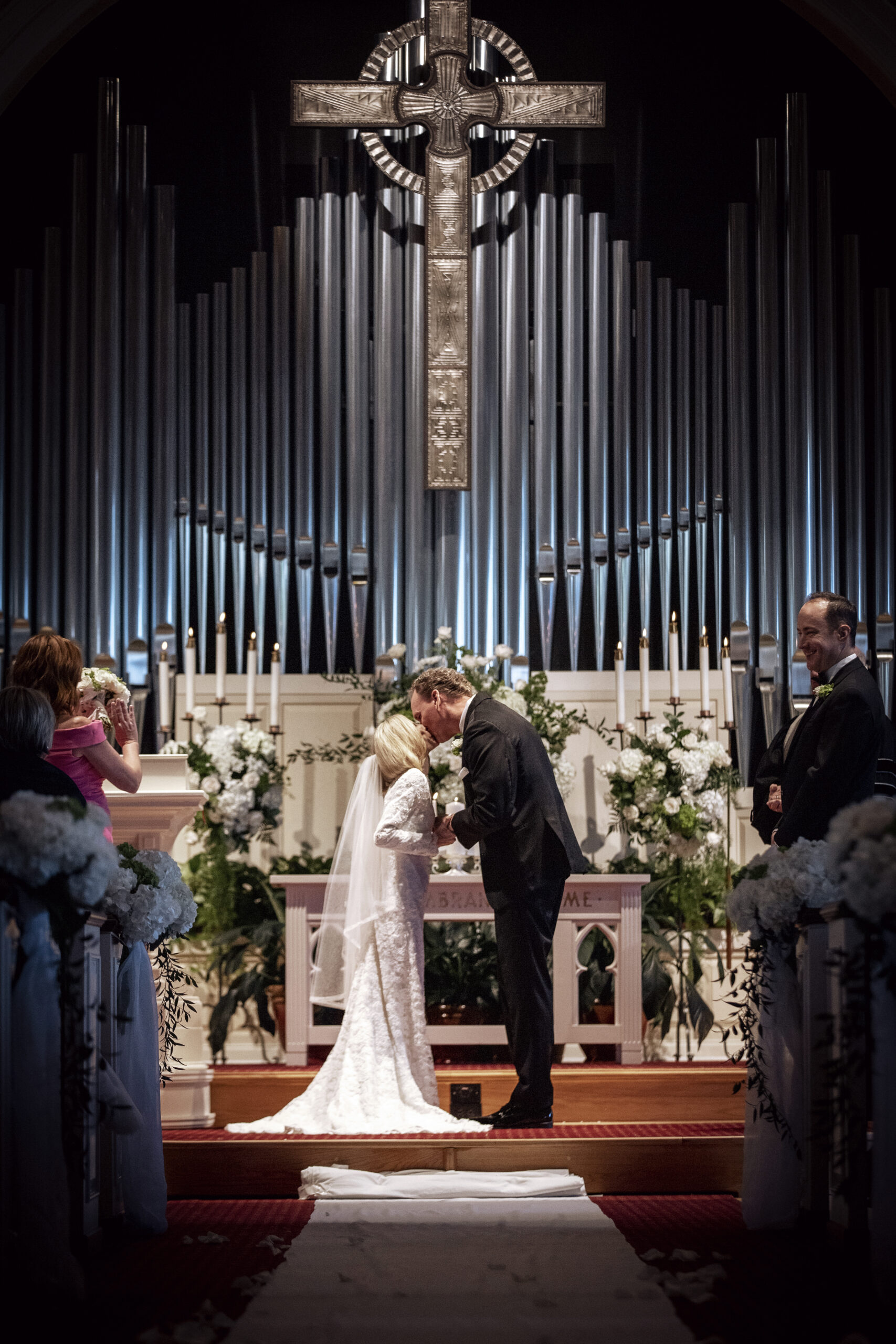 Bride and groom share their first kiss at the altar of The Royal Poinciana Chapel on Palm Beach Island, surrounded by elegant white florals, candlelight, and the grandeur of the church’s iconic organ pipes. Captured by David Scarola Photography, Palm Beach wedding photographer known for timeless, fine-art storytelling and cinematic mastery. A sacred moment of love, light, and reverence — beautifully preserved